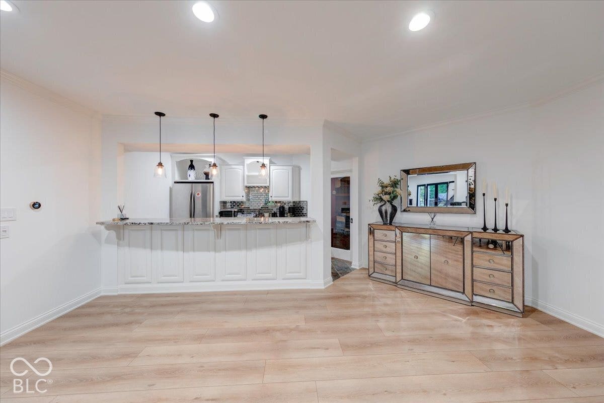 Recessed lighting illuminating wood-finish flooring, a kitchen featuring pendant lighting, white cabinetry, and a stone-finish countertop