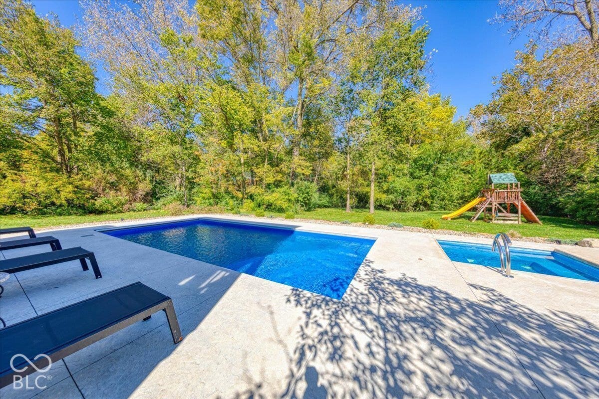 Expansive backyard featuring a large in-ground swimming pool and an integrated hot tub, surrounded by a concrete patio