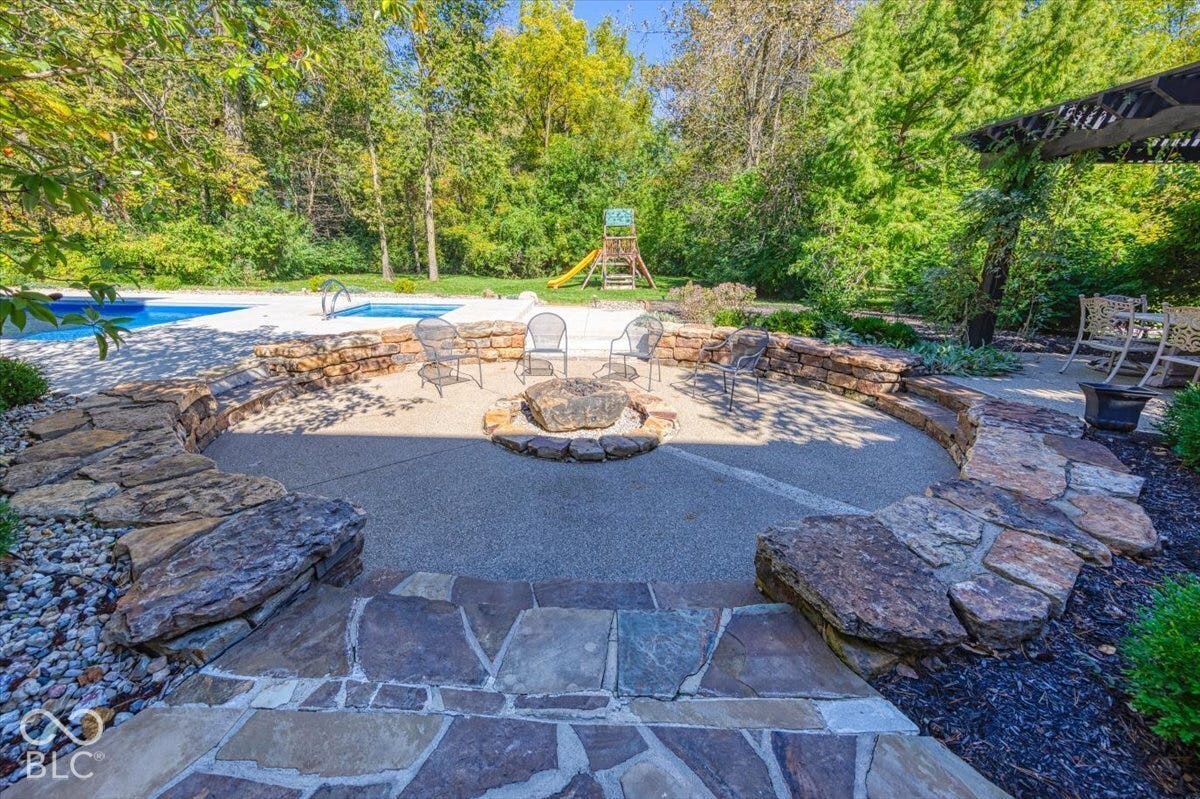 Backyard oasis featuring a circular fire pit with natural stone surround, flagstone patio, and mature landscaping