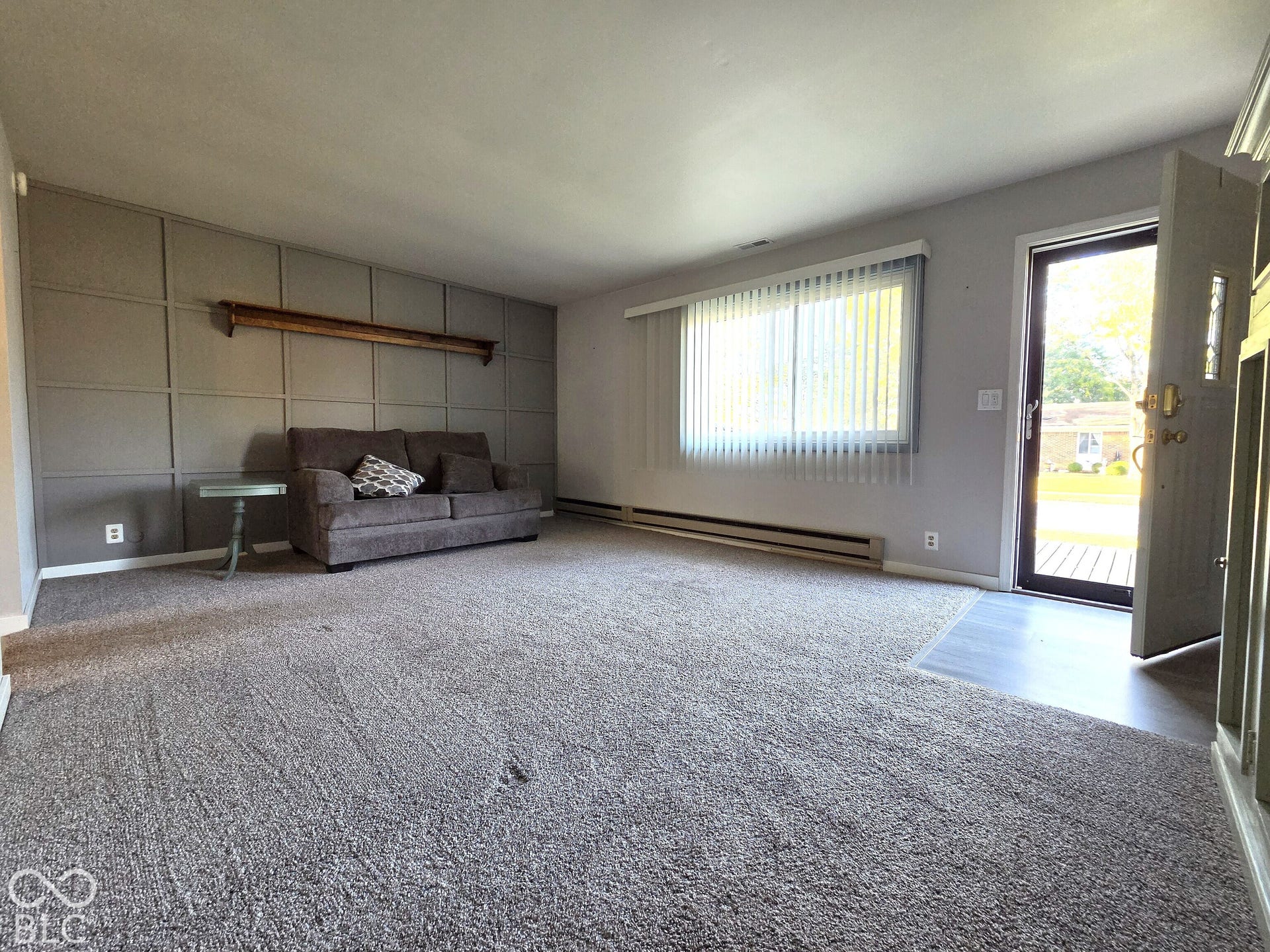 1221 Elk Lane, Elwood, IN 46036 Living area featuring paneled accent wall, wood-finish wall shelving, carpeting, and a window with vertical blinds
