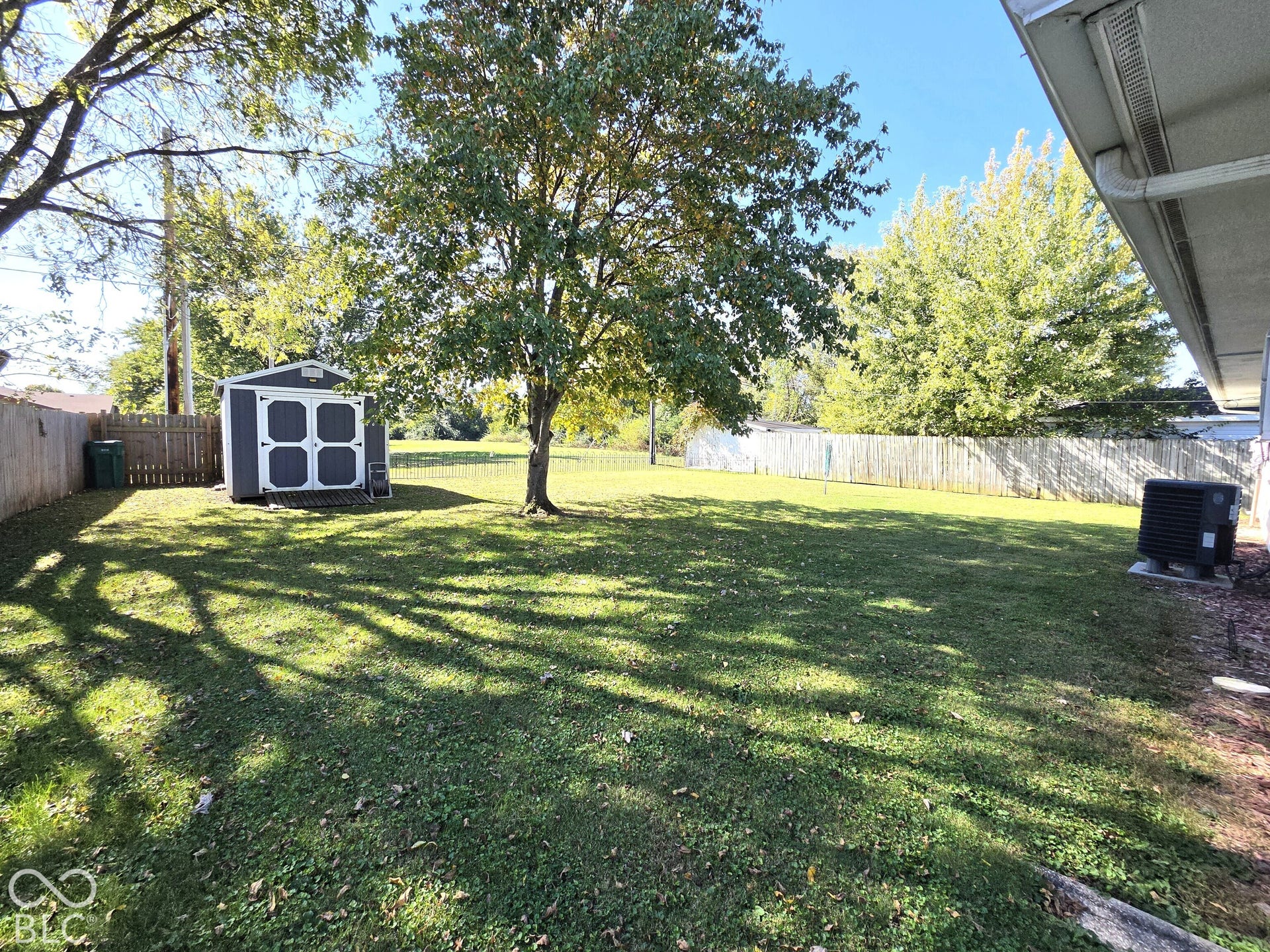 1221 Elk Lane, Elwood, IN 46036 Expansive backyard featuring a lush lawn, mature trees, a storage shed, and a privacy fence