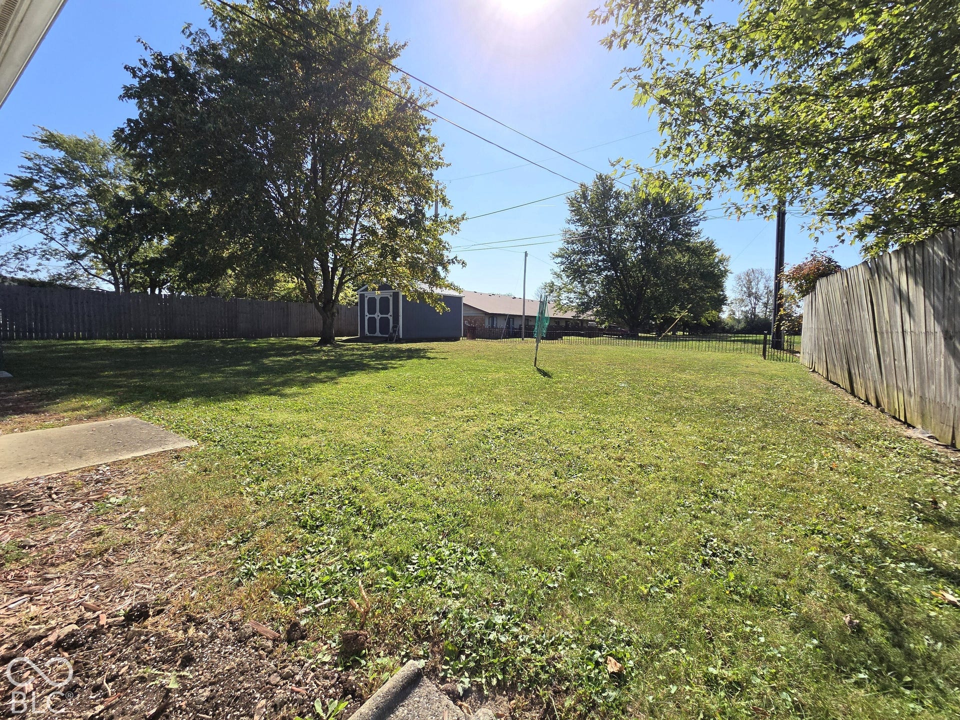1221 Elk Lane, Elwood, IN 46036 Expansive grassy yard with mature trees, a wood privacy fence, and a storage shed