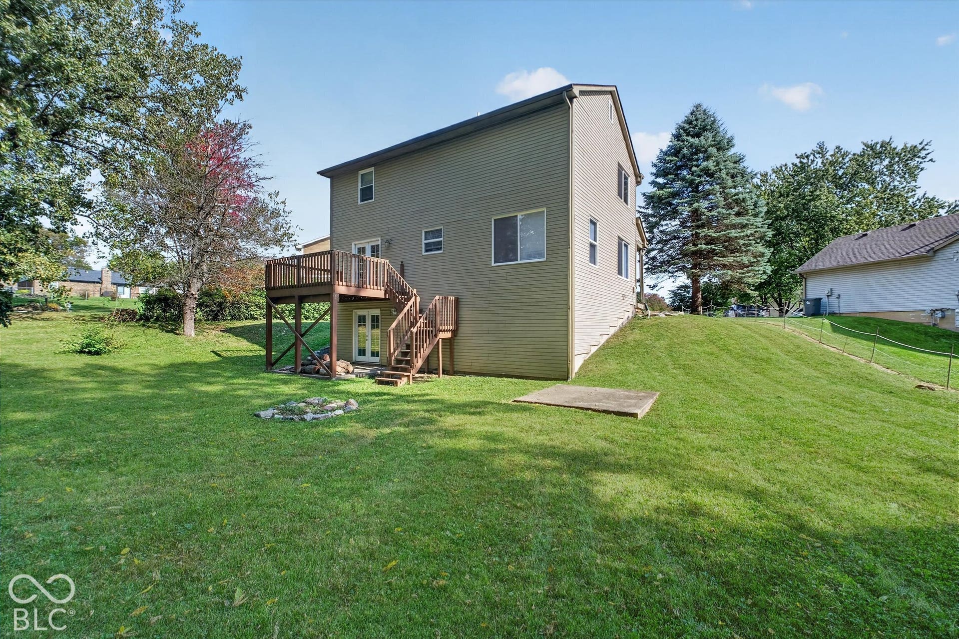 Expansive backyard featuring a wood deck with stairs, double glass doors, and a concrete patio