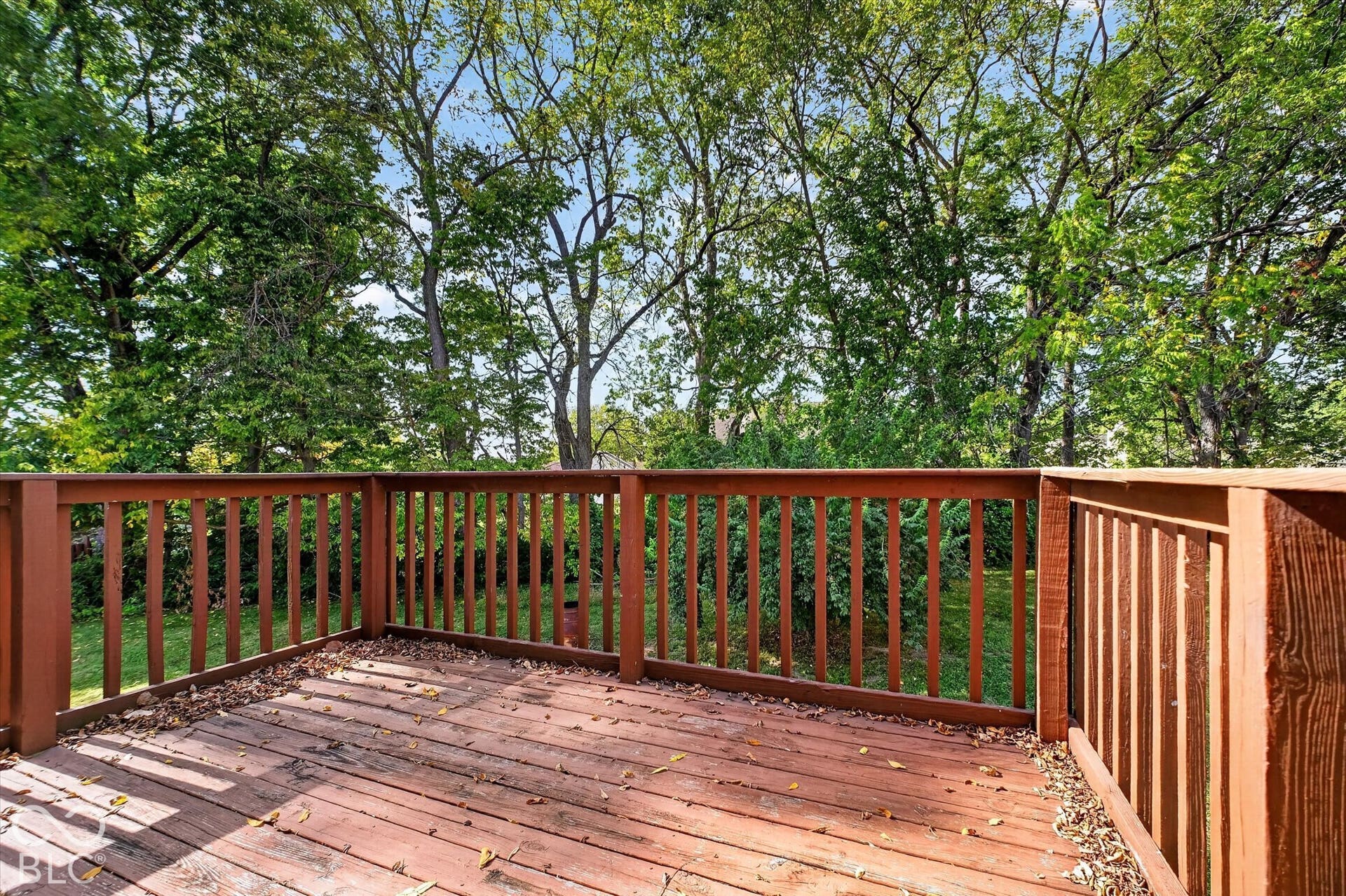 Wood-finish deck with a perimeter railing and mature trees