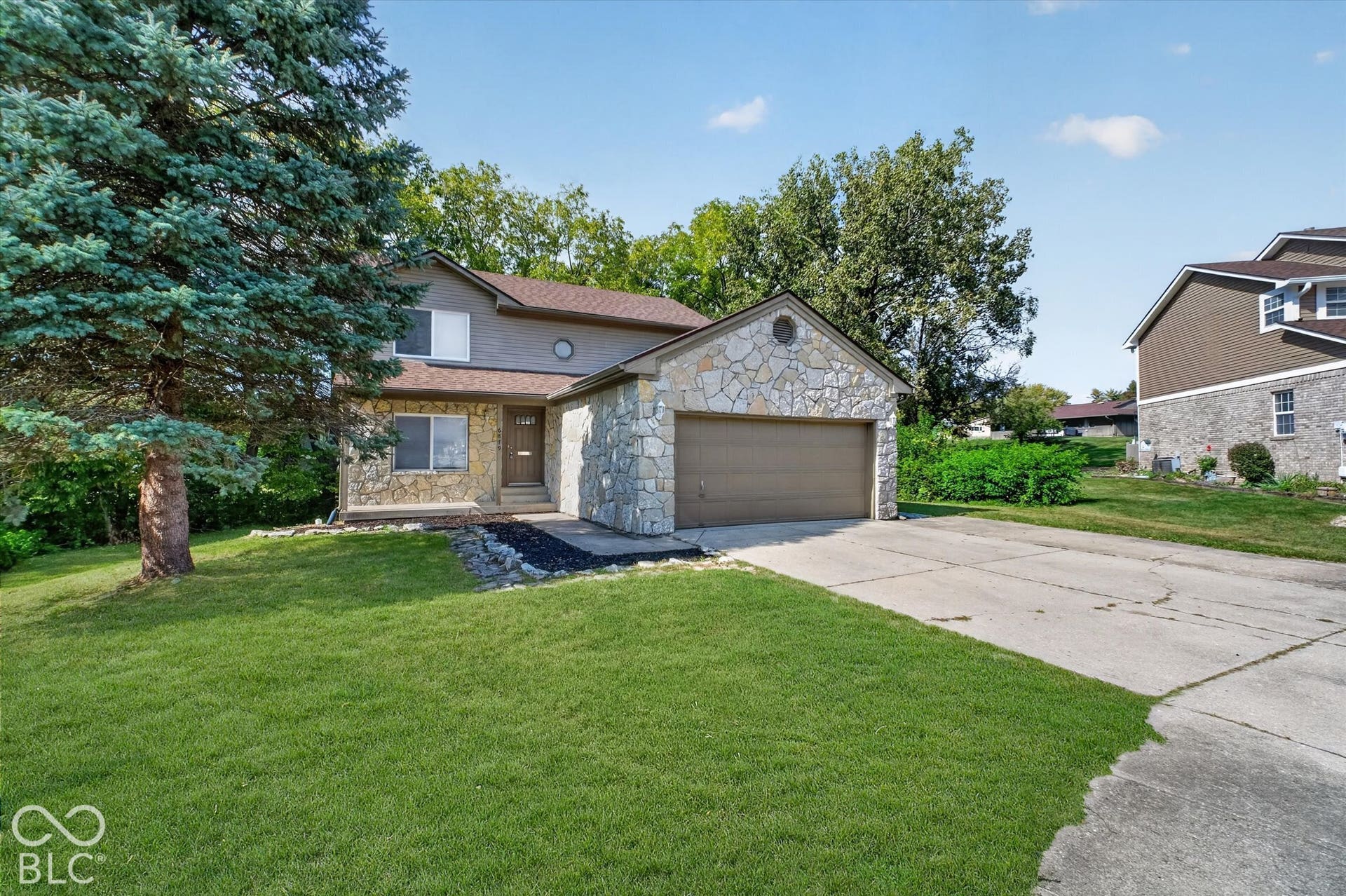 Front of home featuring a paved driveway, attached garage, and spacious front yard