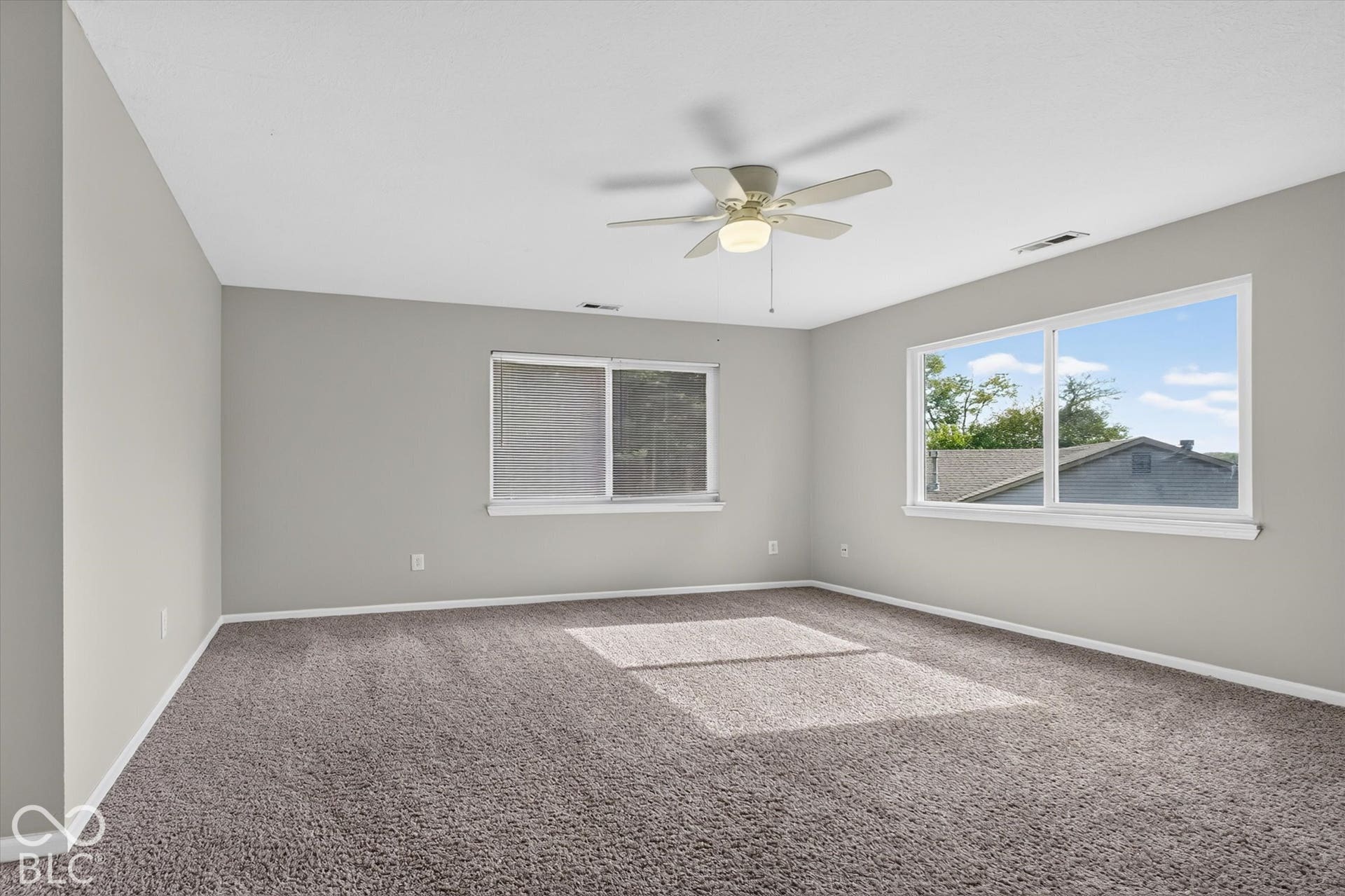 Spacious primary bedroom with carpet, ceiling fan, and abundant natural light