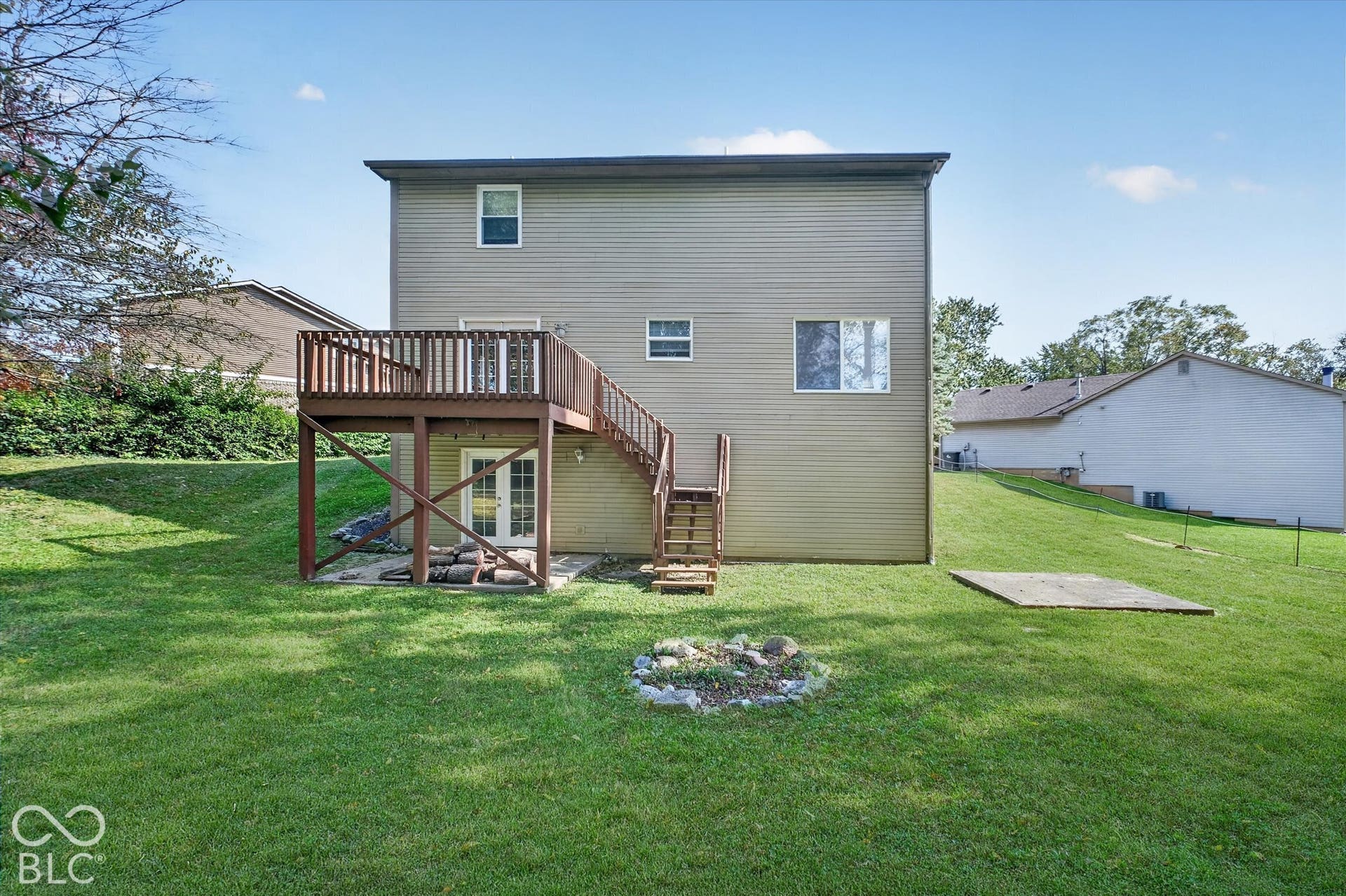 Expansive backyard featuring a wood deck with stairs, double glass doors, and a concrete patio