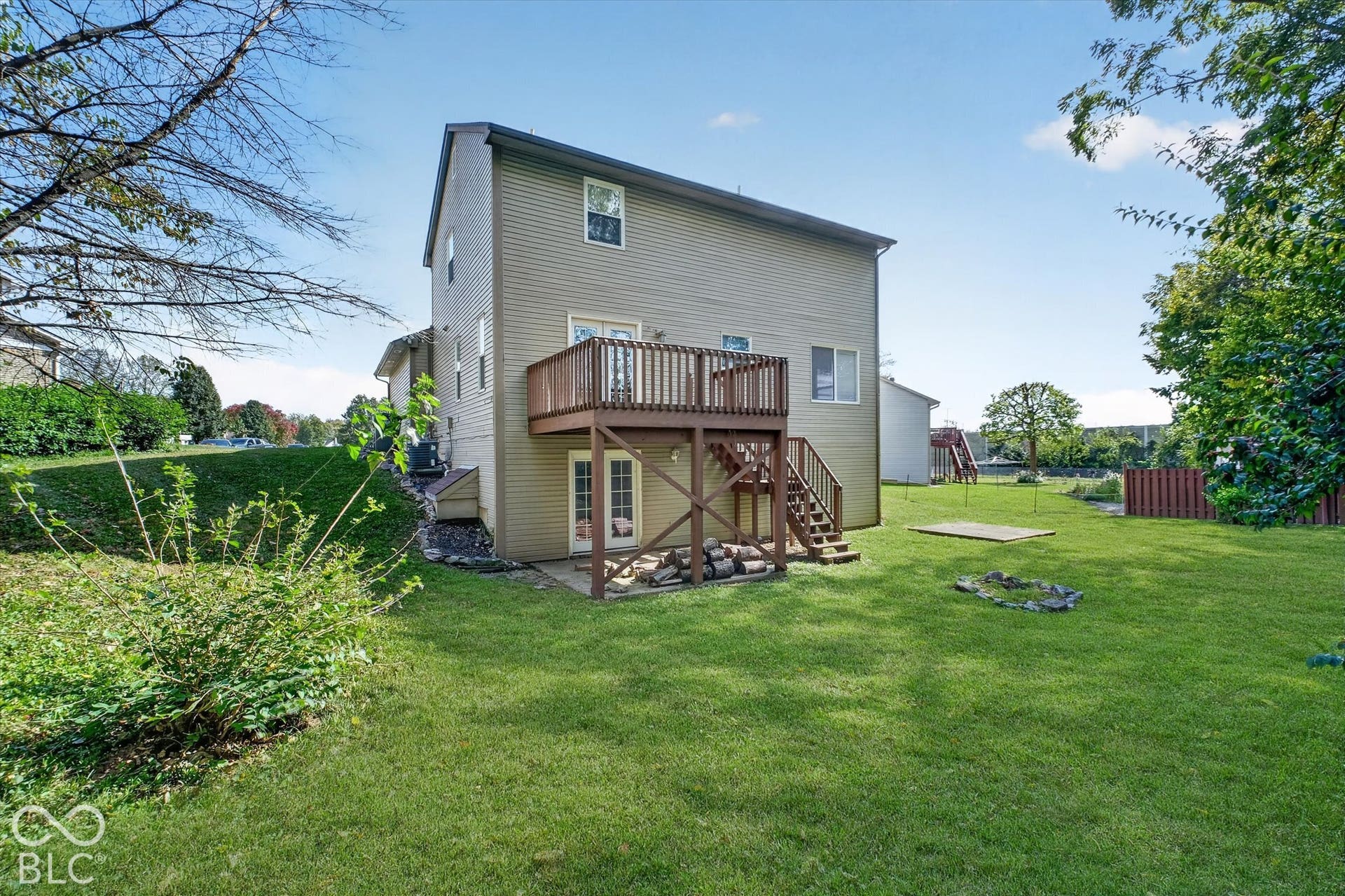 Expansive backyard featuring a wood deck with stairs, double glass doors, and a concrete patio