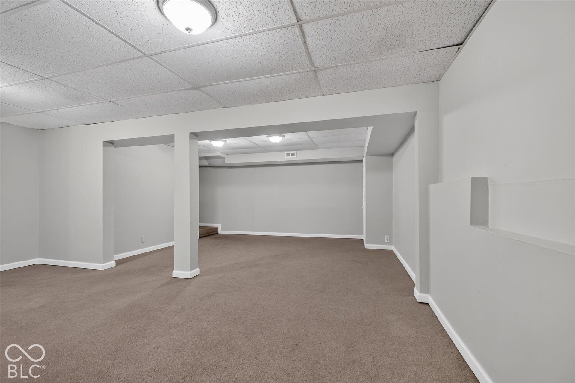 Expansive finished basement with carpeted flooring and neutral wall color