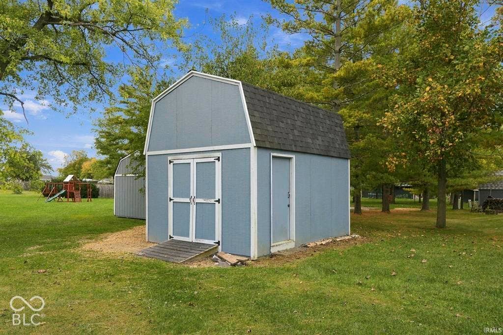 Charming storage shed featuring a classic barn-style roof with dark shingle finish, light blue exterior siding with white trim accents, and dual white paneled doors