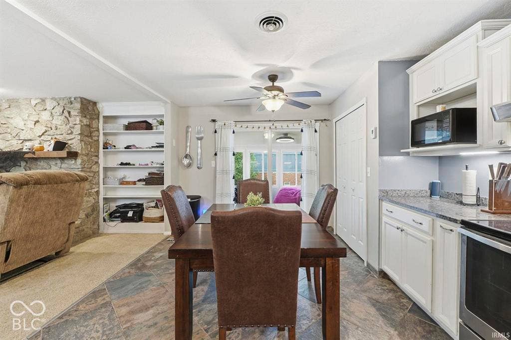 Open-concept kitchen and dining area featuring white cabinetry with integrated appliances, granite countertops, pendant lighting over the dining table, and hardwood-finish flooring throughout