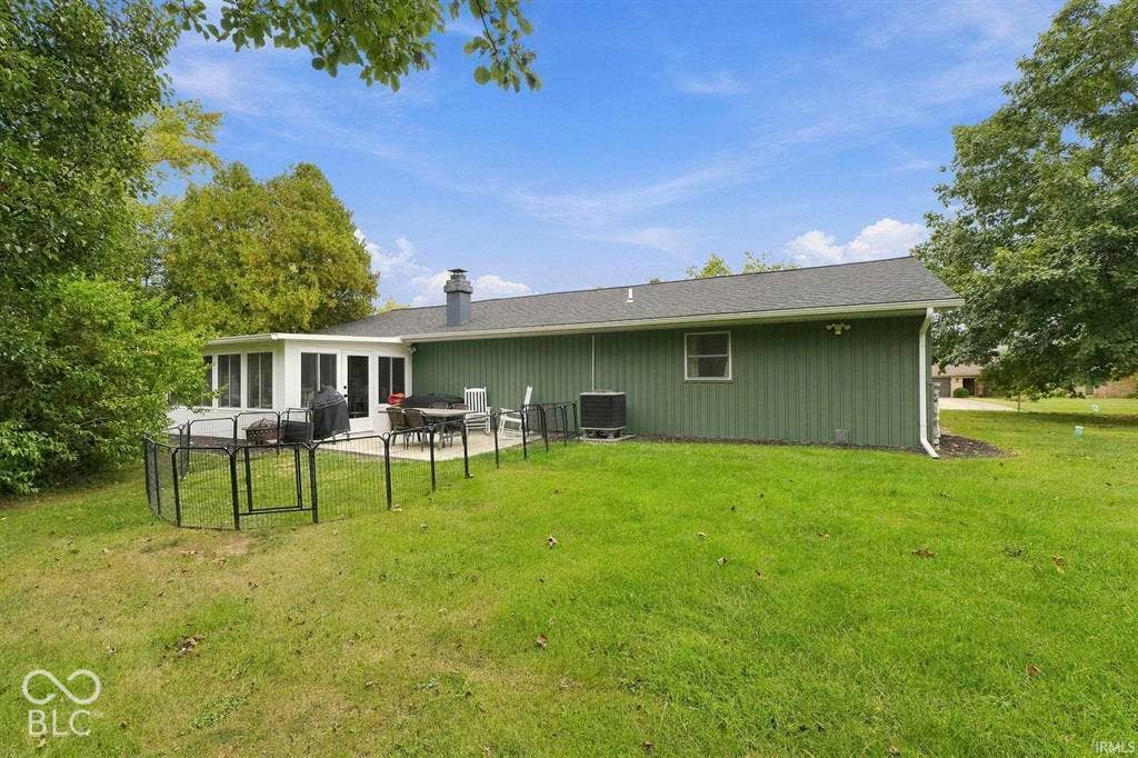 Rear exterior featuring green vertical siding, a sunroom with white-framed windows, a concrete patio, and a dark shingle roof