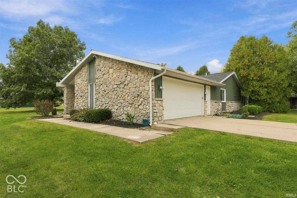 Modern stone and siding exterior with a spacious attached garage, set on expansive manicured grounds surrounded by mature landscaping and established trees