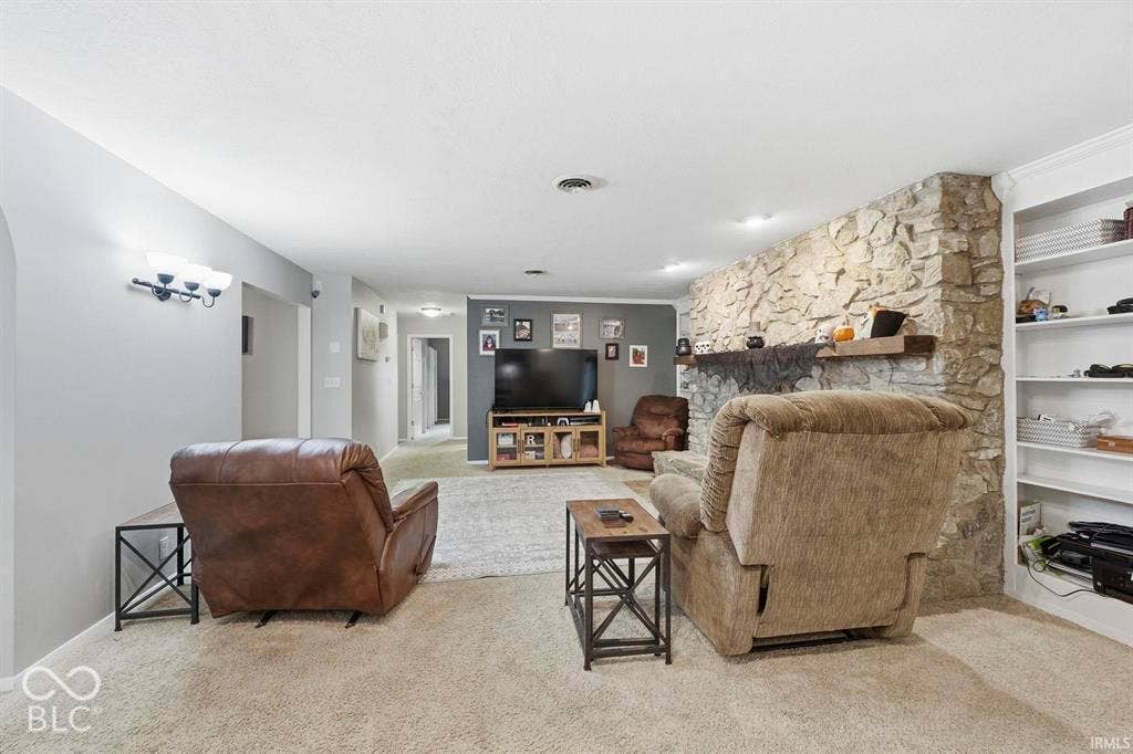 Stone-faced fireplace with a wood mantle, built-in shelving, carpet flooring, and recessed lighting