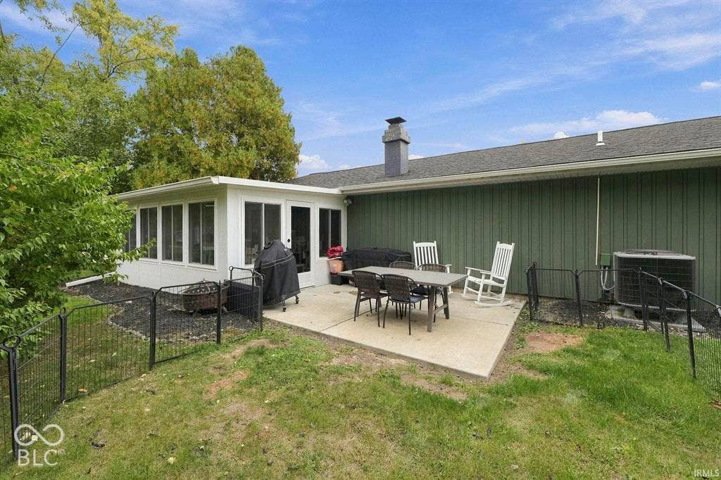 Rear exterior with a concrete patio, board and batten siding, sunroom addition, and fenced garden area