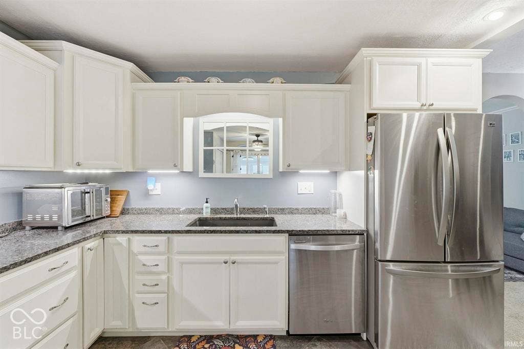 Modern kitchen featuring crisp white cabinetry with brushed nickel hardware, granite countertops with coordinating backsplash, stainless steel appliances including a French-door refrigerator and dishwasher, and an undermount sink with a professional-grade faucet