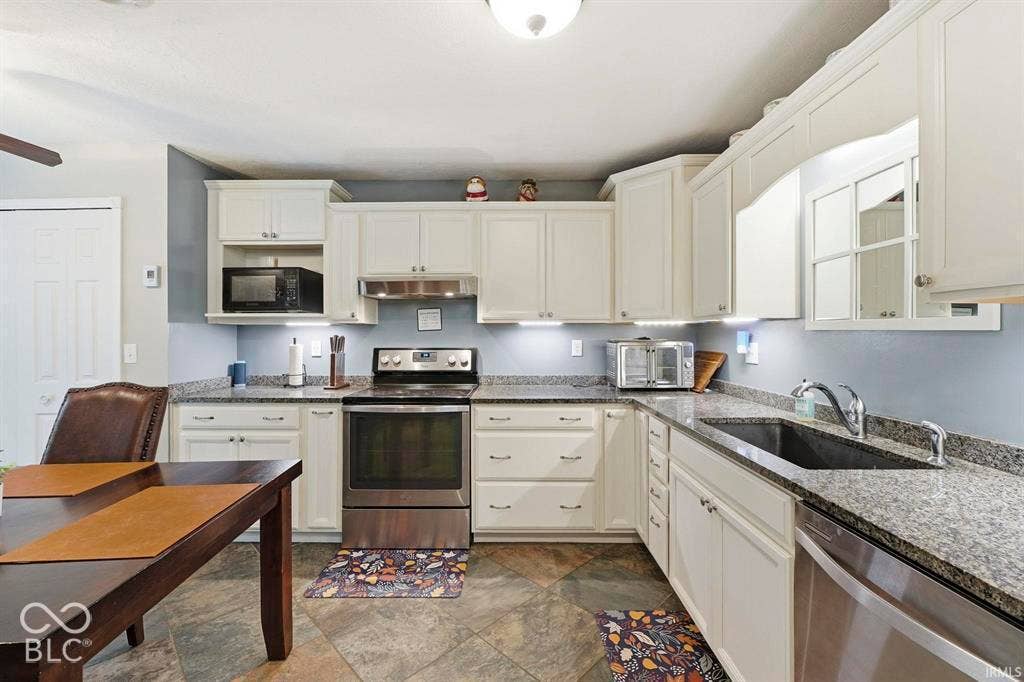 White cabinetry, stone countertops, stainless steel appliances, undermount sink, and tiled flooring