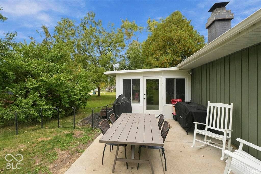 Expansive composite deck with composite decking and dining table seating, leading to a contemporary single-story residence featuring board-and-batten siding, metal roof with chimney, and large sliding glass doors