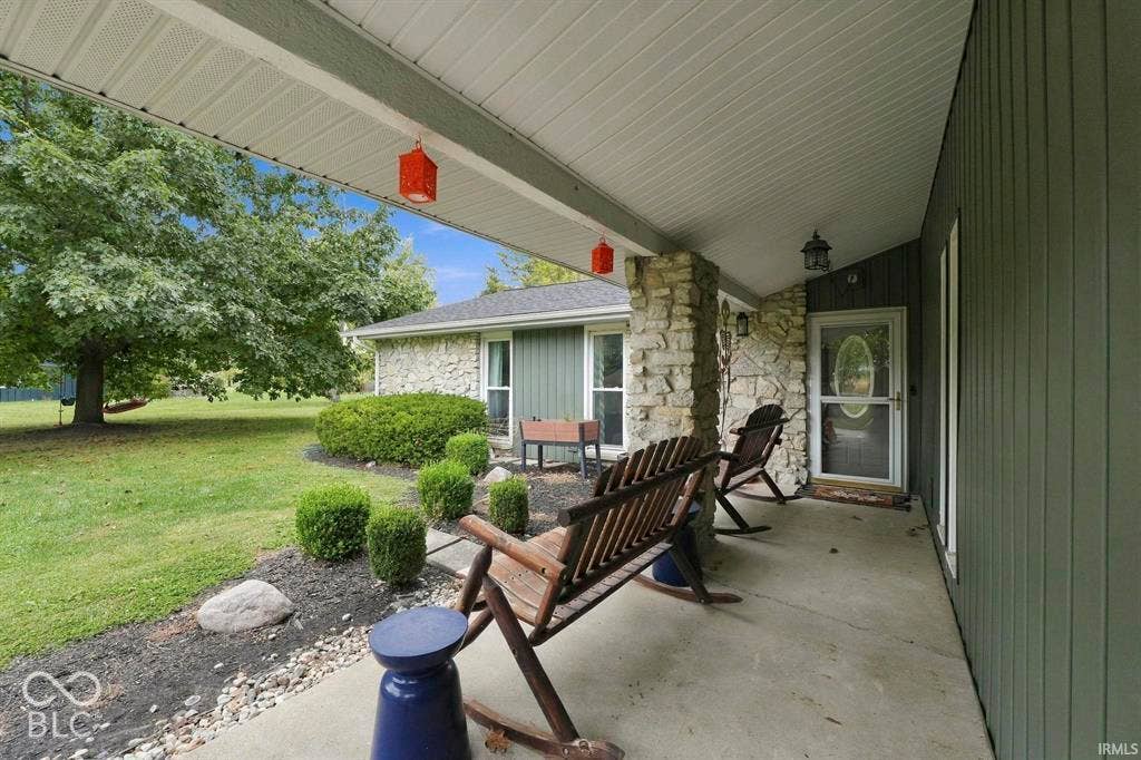 Expansive covered porch with stone and corrugated metal siding, featuring Adirondack seating and a blue accent table