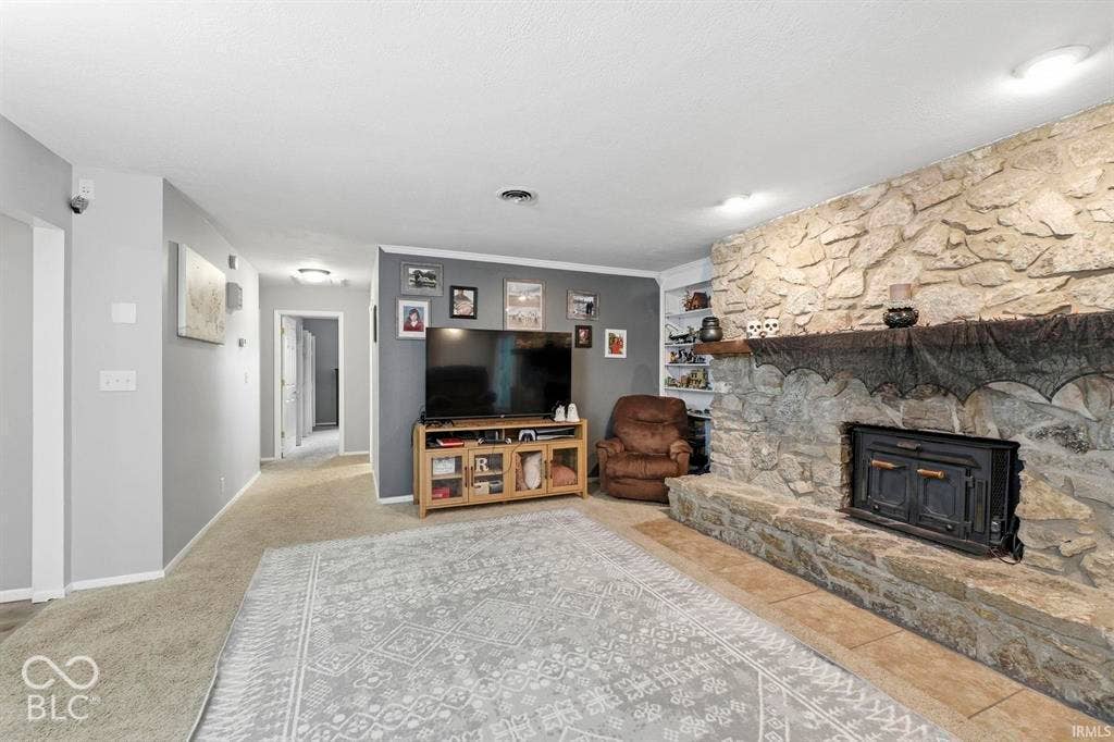 Spacious basement recreation room featuring exposed stone fireplace with wood-burning stove insert, built-in wooden media console, neutral tile and wood-finish flooring, and recessed ceiling lighting throughout