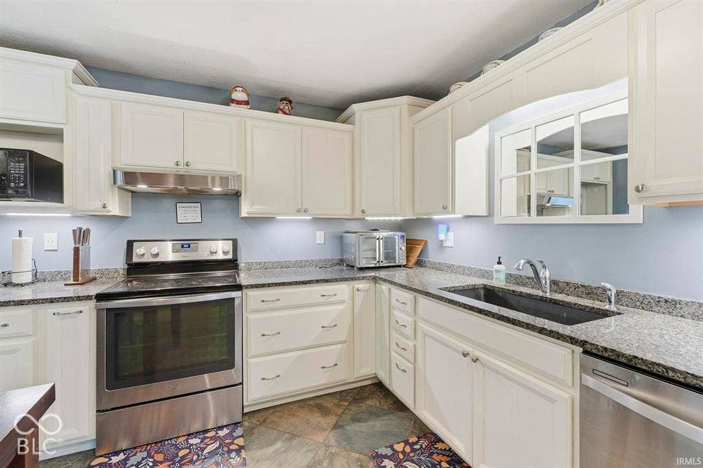 Bright kitchen featuring cream cabinetry with brushed nickel hardware, stainless steel appliances including a convection range and dishwasher, speckled granite countertops, undermount sink with chrome faucet, and tile backsplash