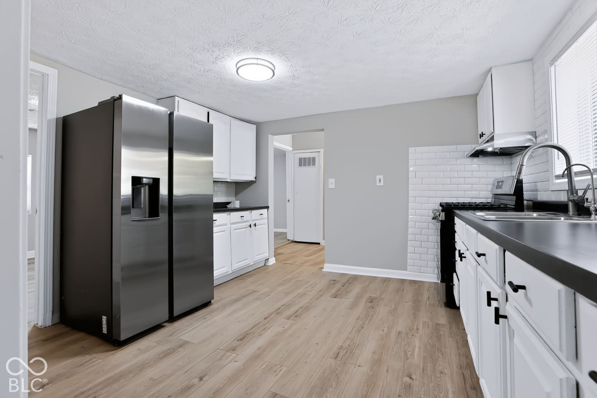 Kitchen featuring wood-finish flooring, white cabinetry, dark countertops, a subway tile backsplash, and a stainless steel side-by-side refrigerator