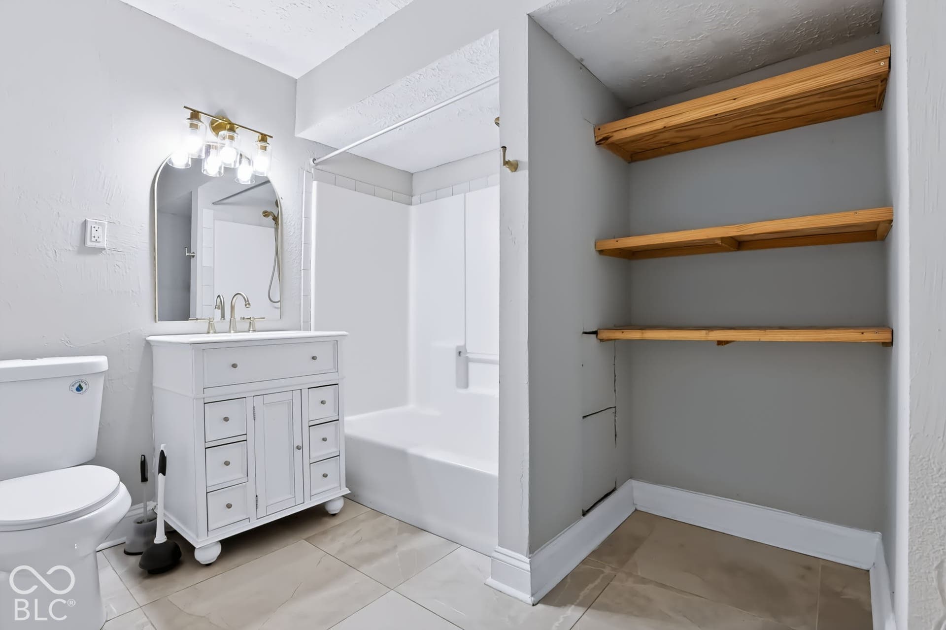 White vanity with ample storage, an arched mirror, and a gold-tone light fixture