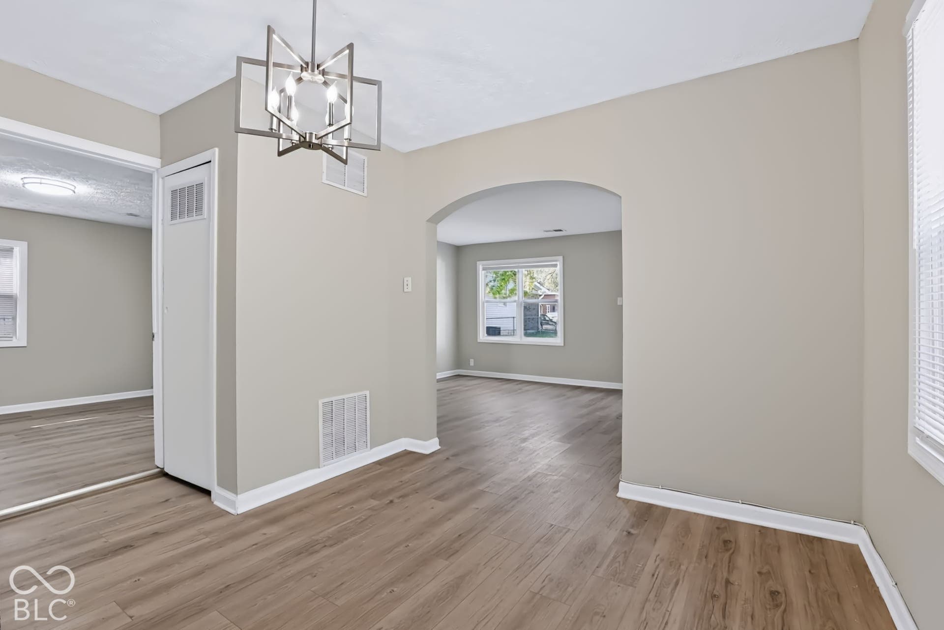 Wood-finish flooring throughout, arched doorway, contemporary geometric chandelier, and white window blinds