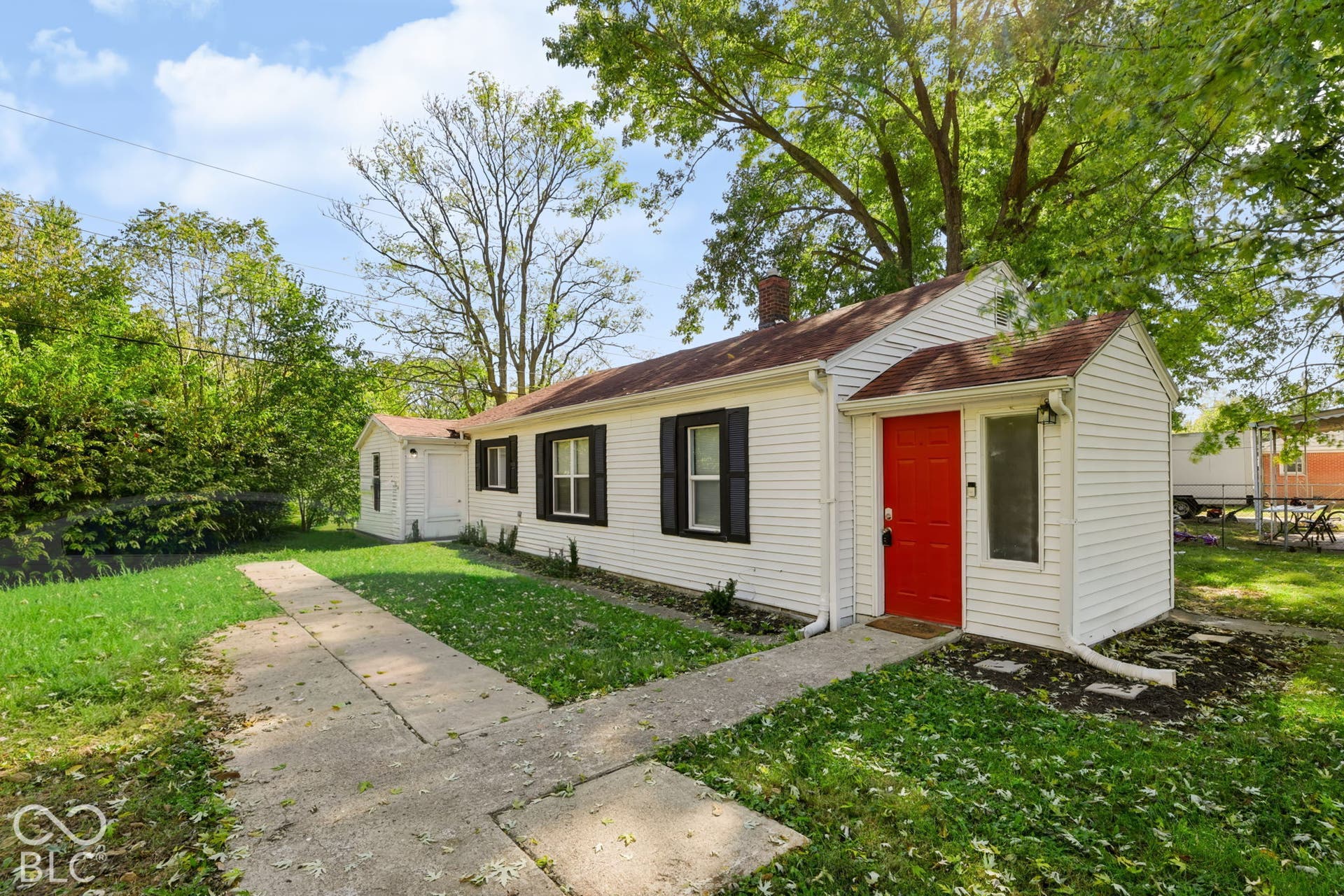 White siding exterior with a red entry door, black window shutters, and a concrete pathway