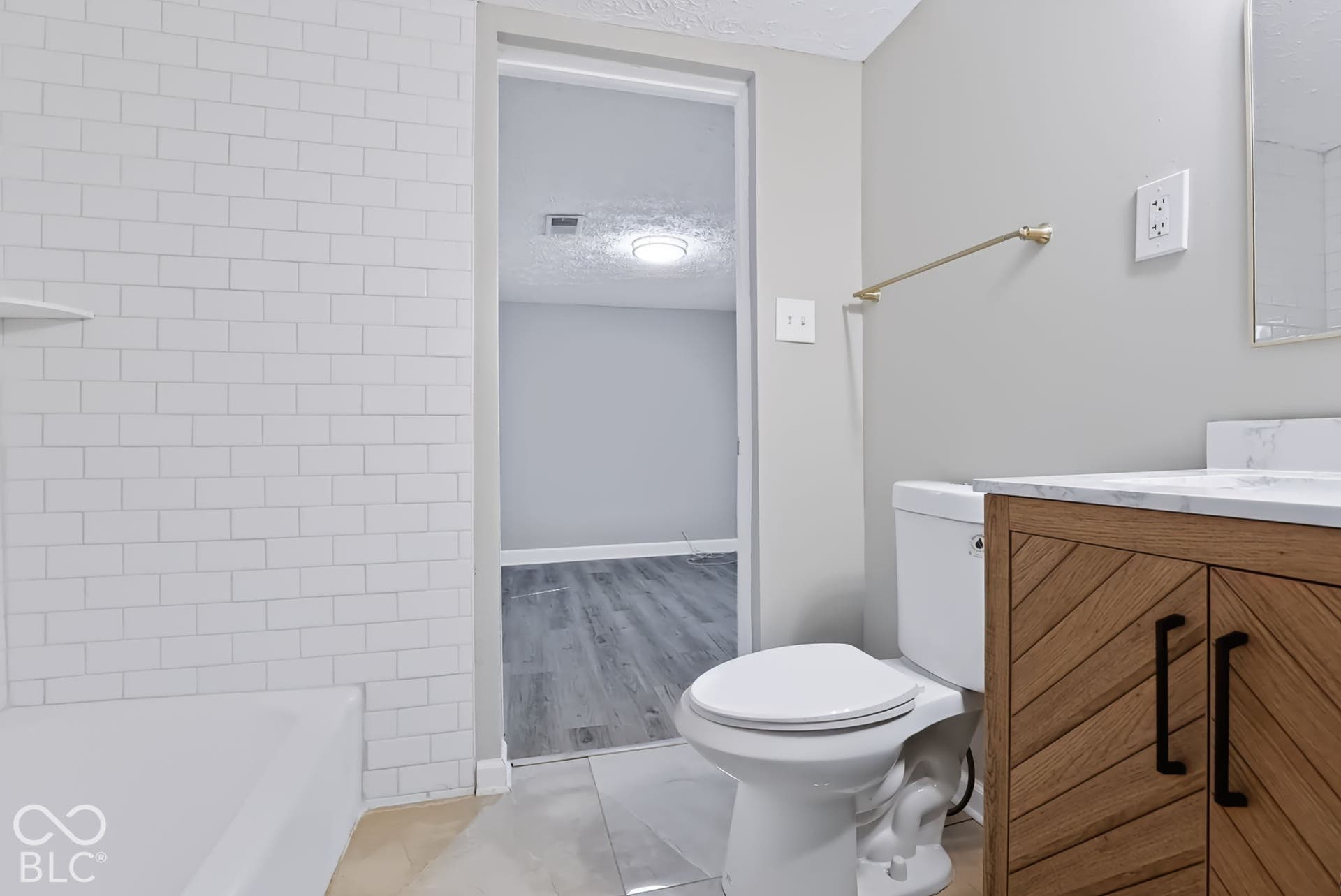 Bathroom featuring white subway tile surround, a wood-finish vanity with black hardware, and a light-toned countertop