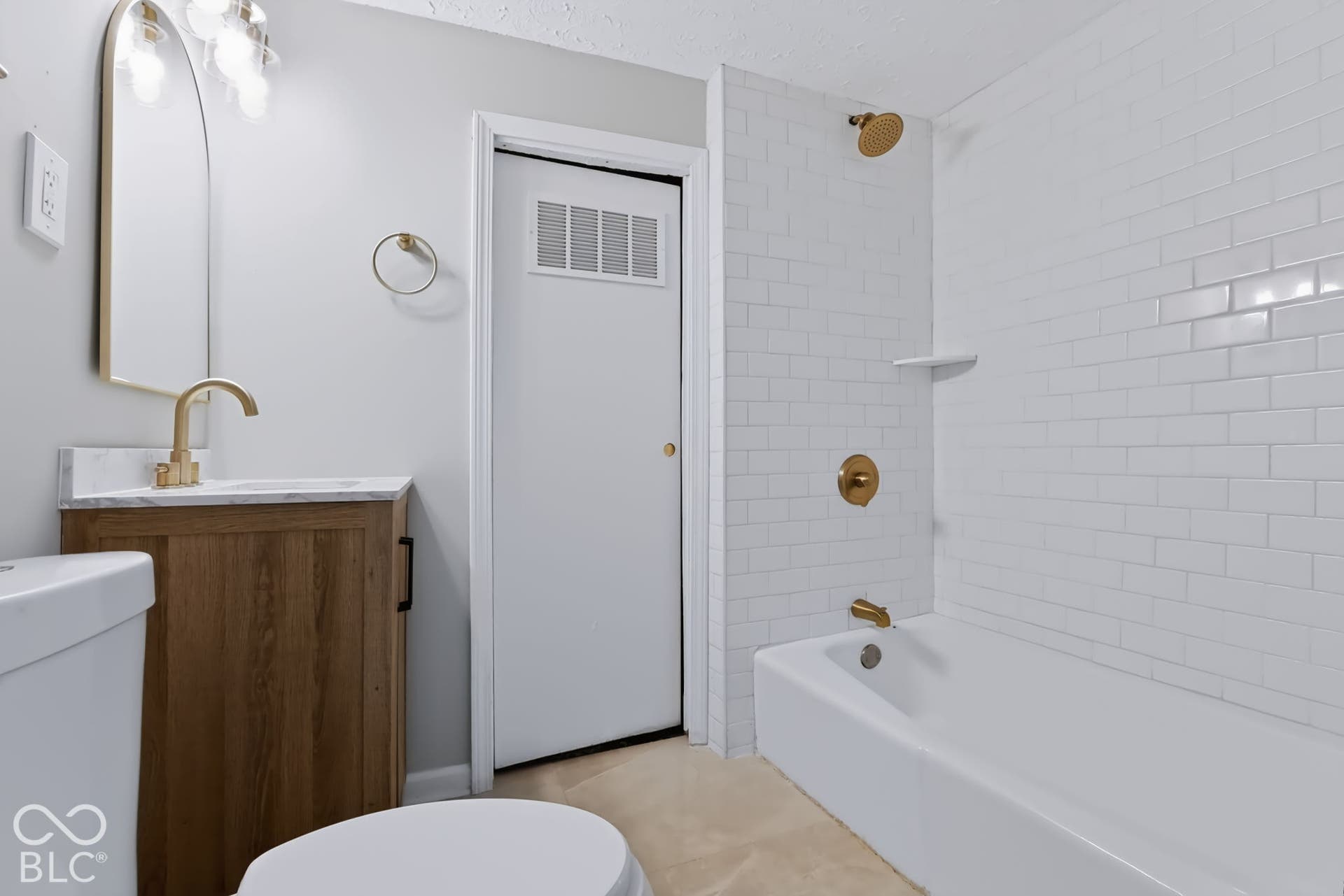 White subway tile shower surround with a built-in shelf, gold-finish fixtures, and a white bathtub