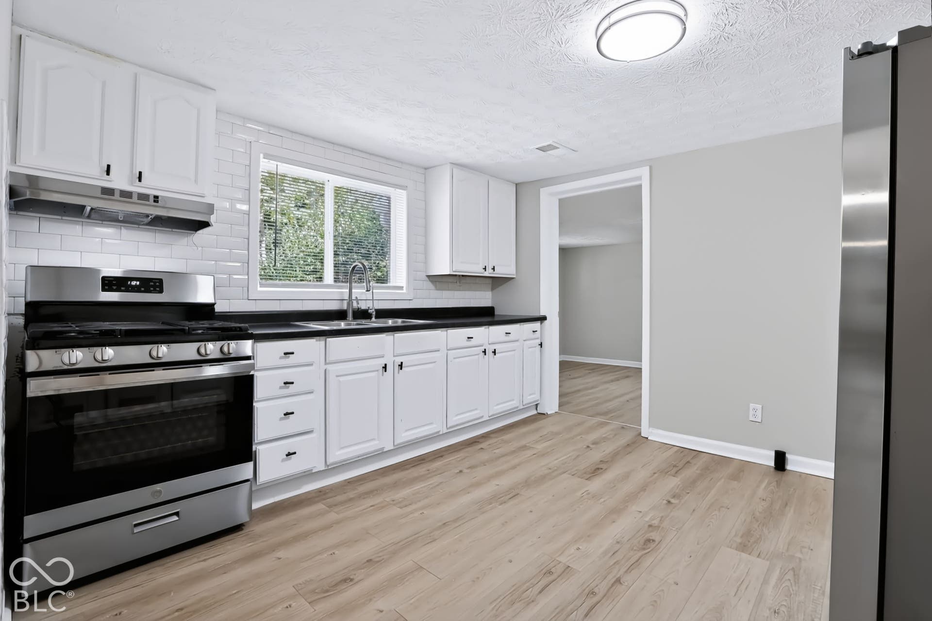 Kitchen featuring white cabinetry, black countertops, stainless steel appliances, white subway tile backsplash, and wood-finish flooring