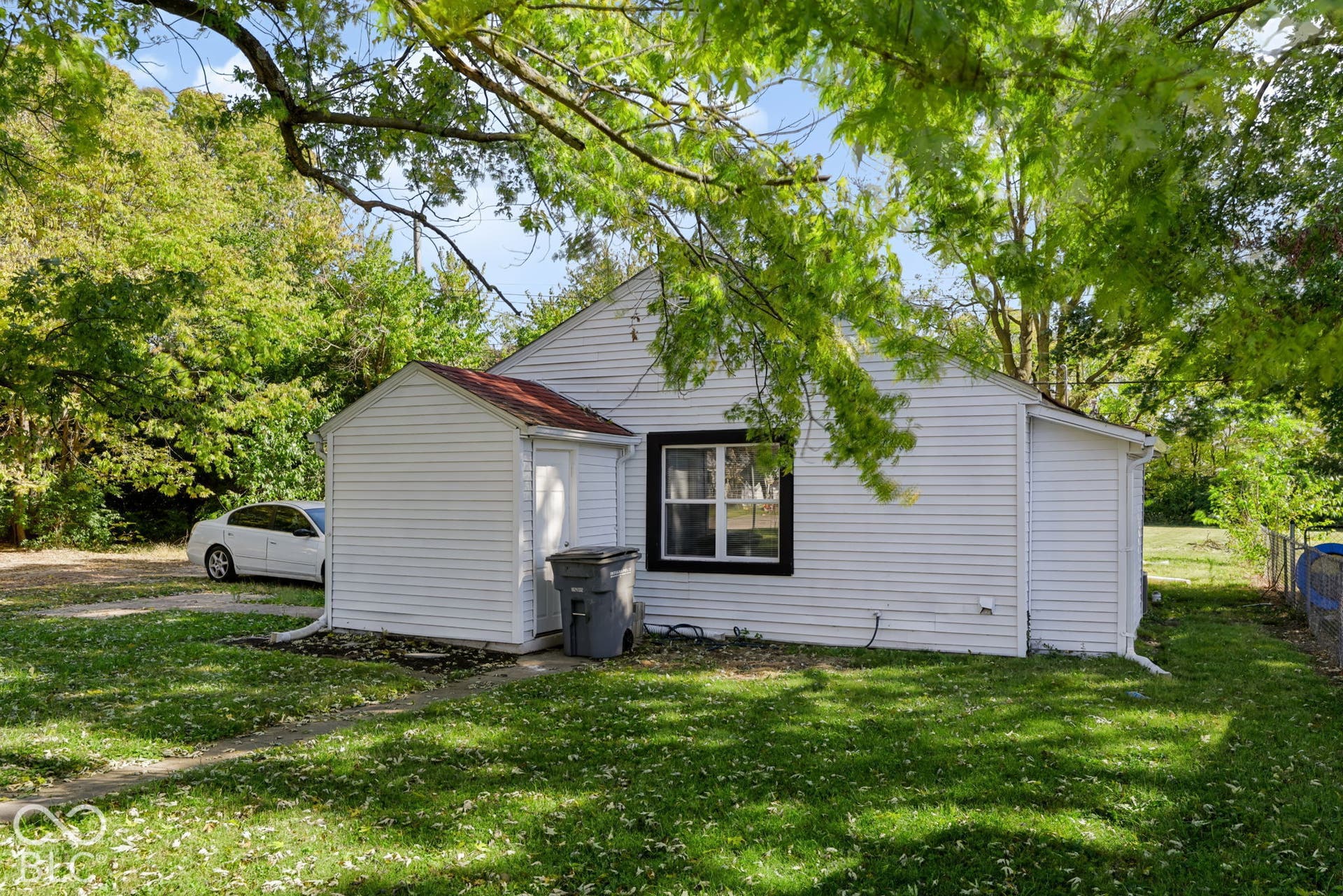 White siding exterior with a dark-trimmed window, a white downspout, and a small attached shed with a red roof