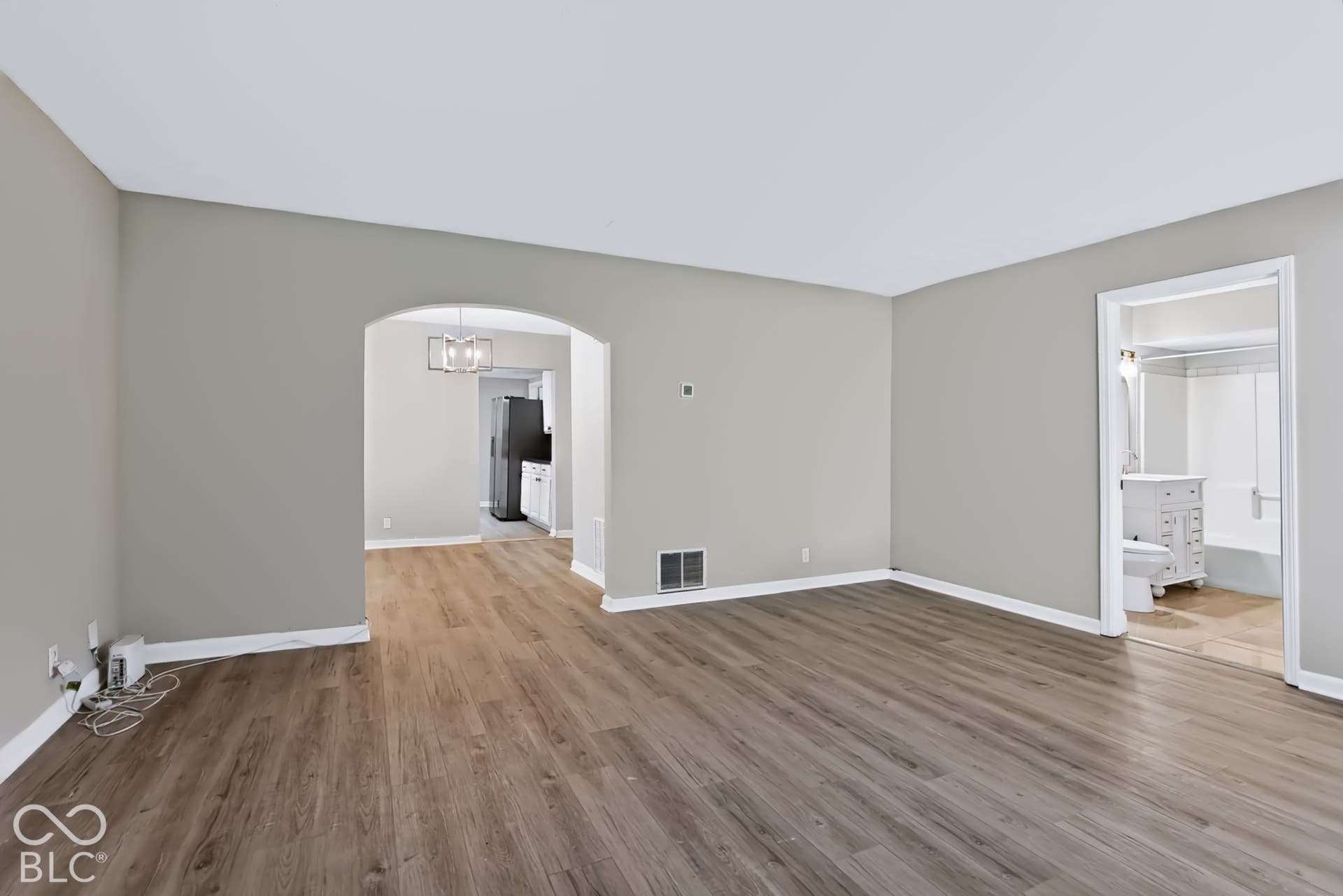 Wood-finish flooring throughout, light gray wall paint, white trim, and an arched doorway leading to a separate room