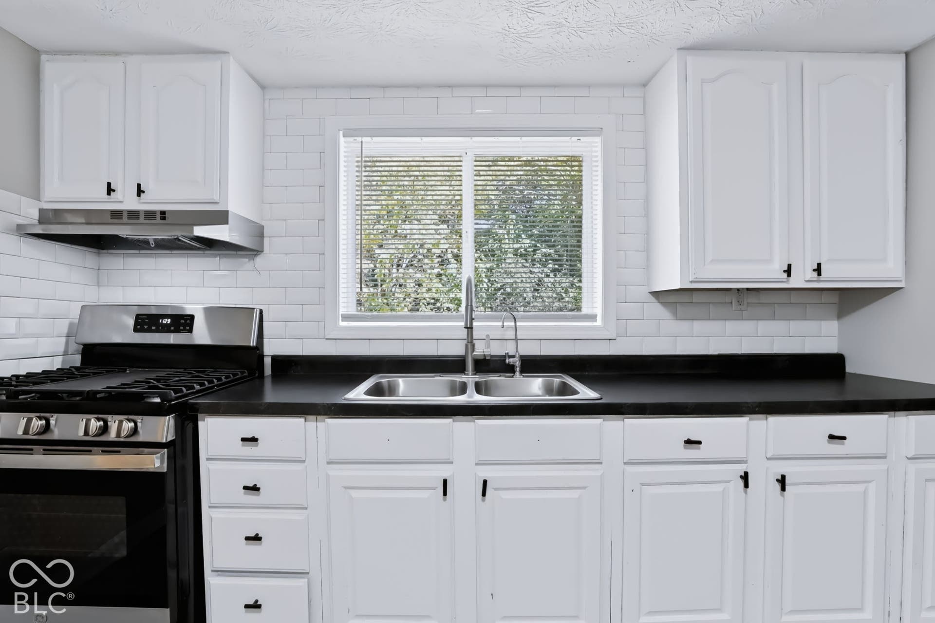 White cabinetry, subway tile backsplash, stainless steel gas range, stainless steel range hood, and a double basin sink