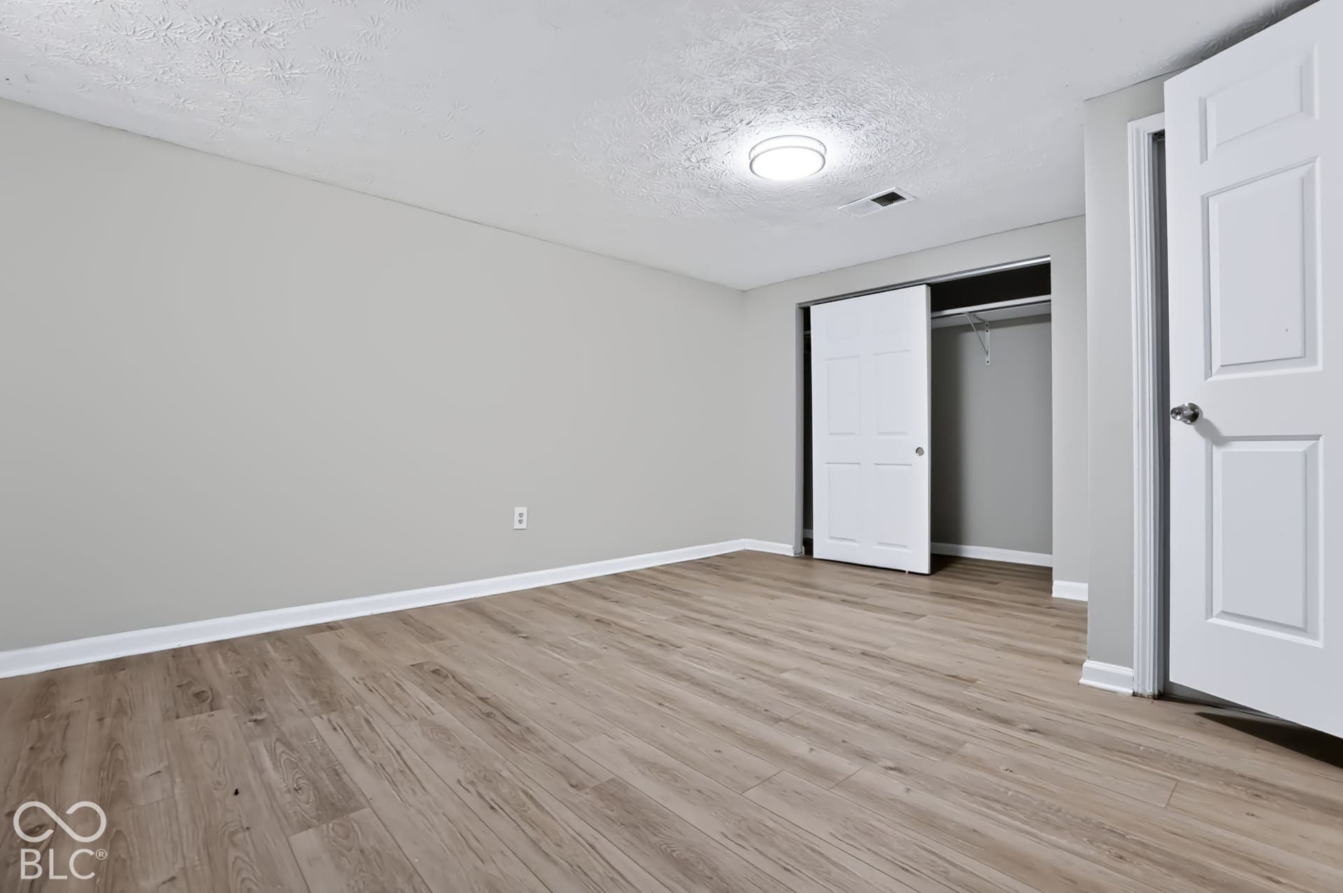 Wood-finish flooring, neutral wall paint, overhead flush-mount lighting, and a closet with bi-fold doors