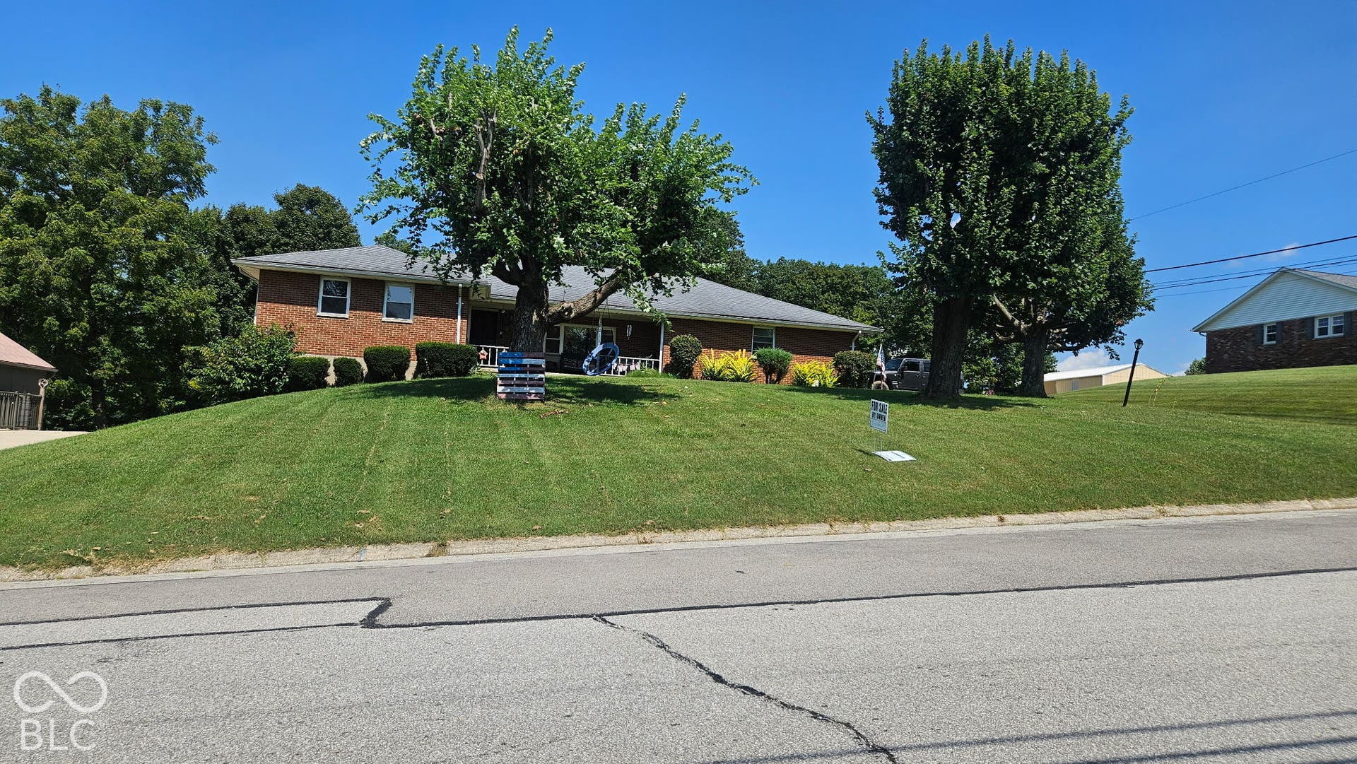 Brick facade residence with a pitched roof, front yard with mature trees, and landscaped shrubbery