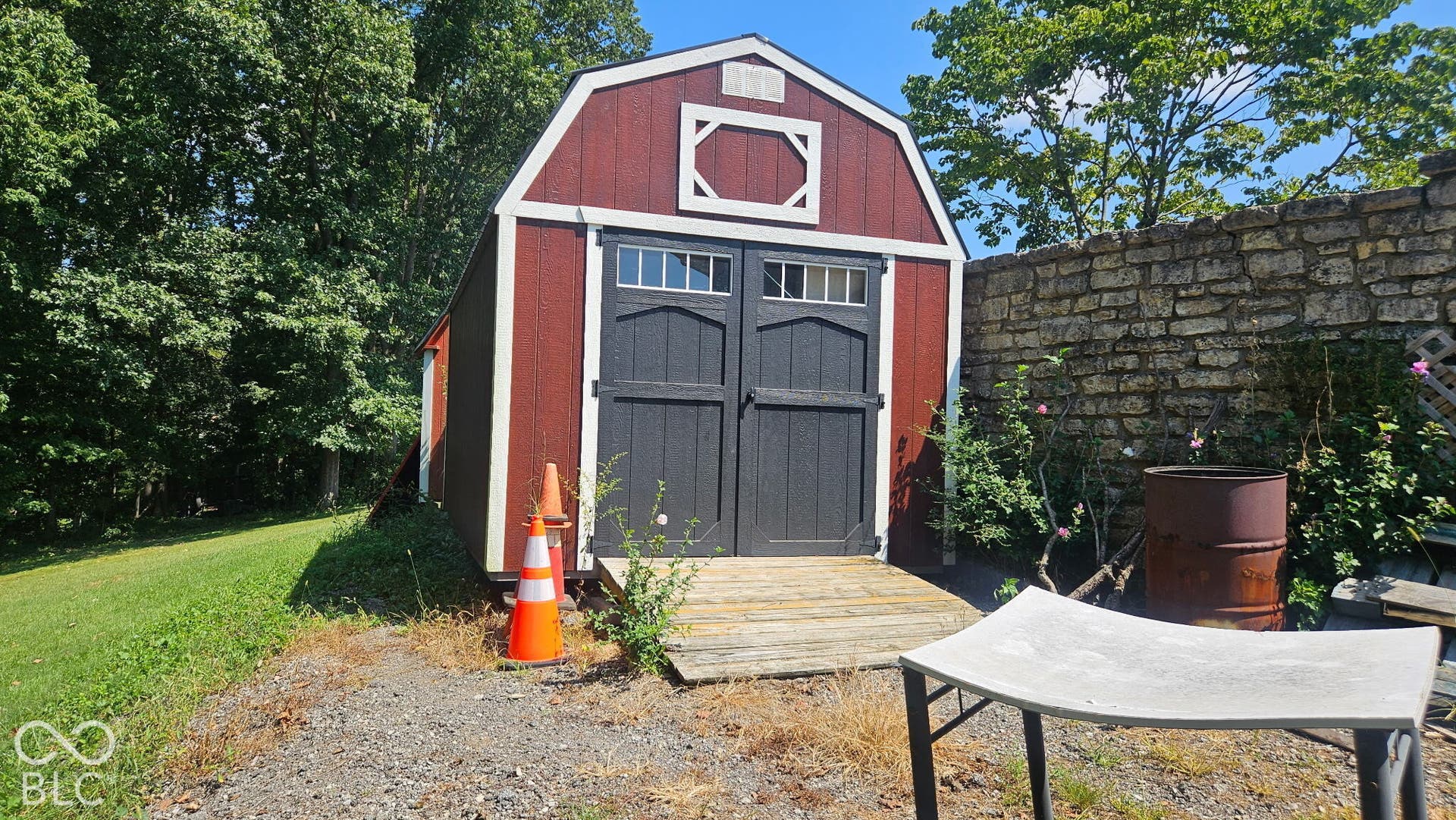 Red barn-style shed with white trim, dark gray double doors, and a wood ramp