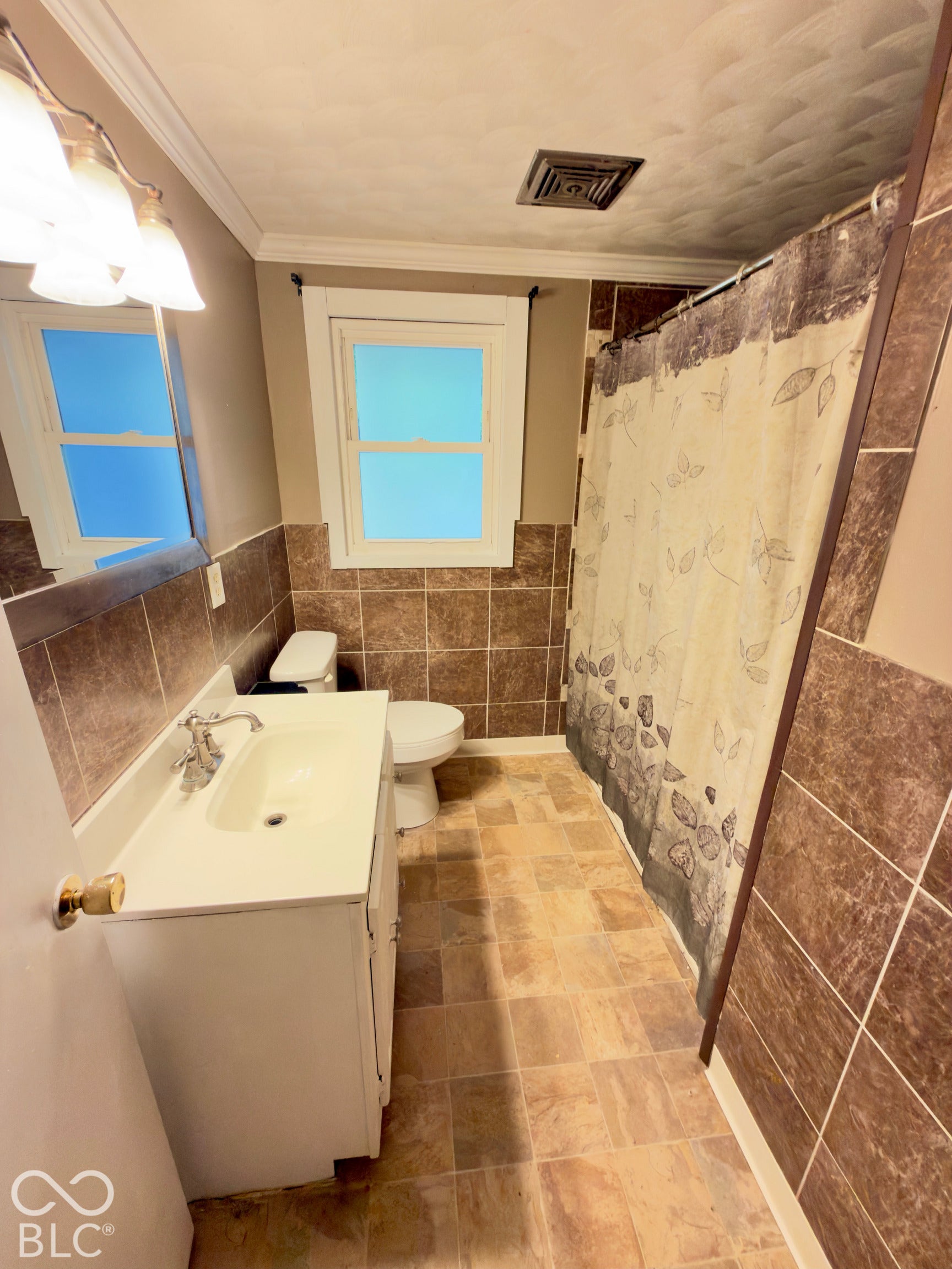 Bathroom featuring square-tiled wall surrounds, a white vanity cabinet, an integrated sink basin with chrome faucet hardware, and a window with white trim