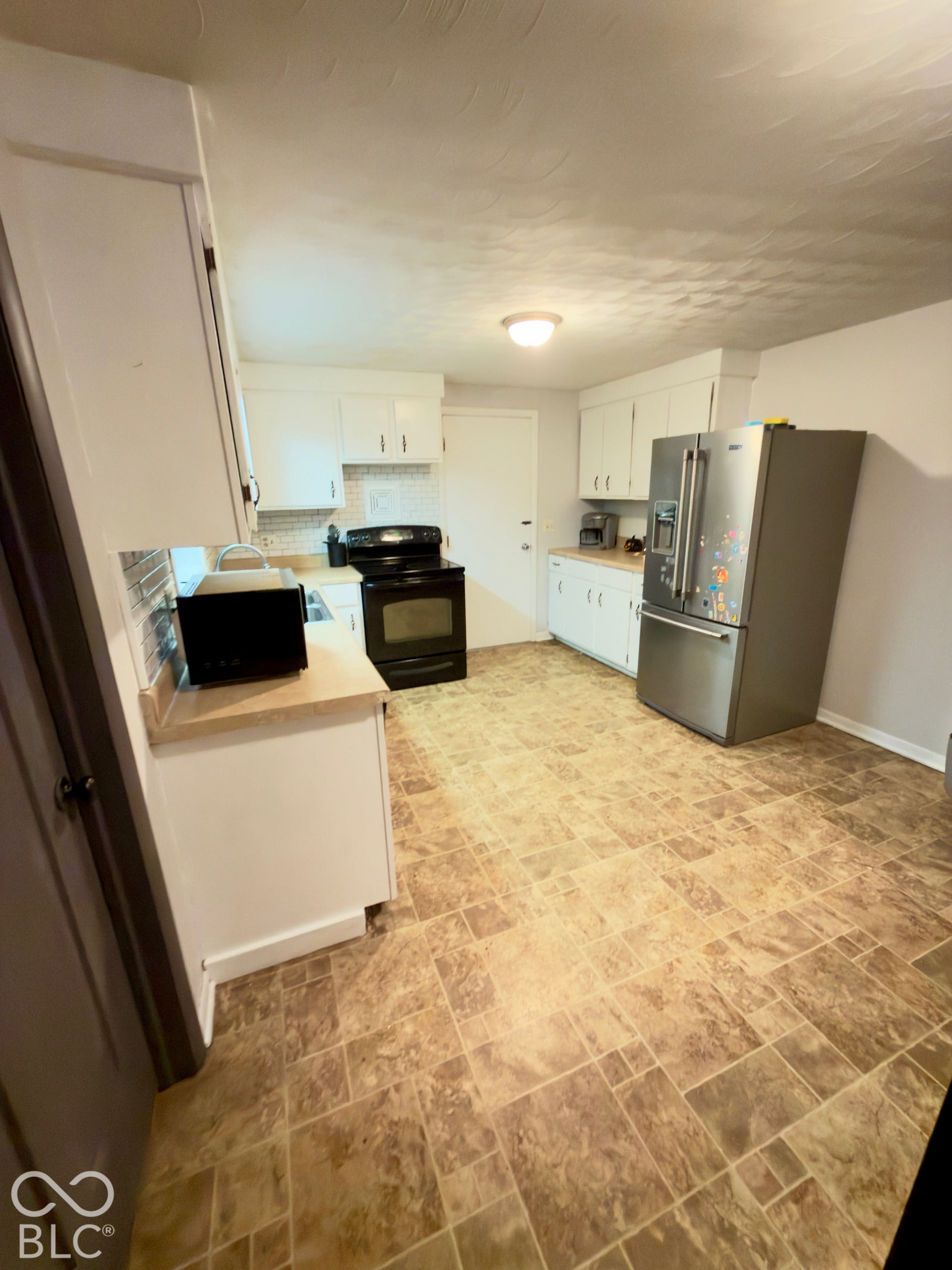 Kitchen featuring white cabinetry, solid-surface countertops, tile backsplash, stainless steel refrigerator, and tiled flooring