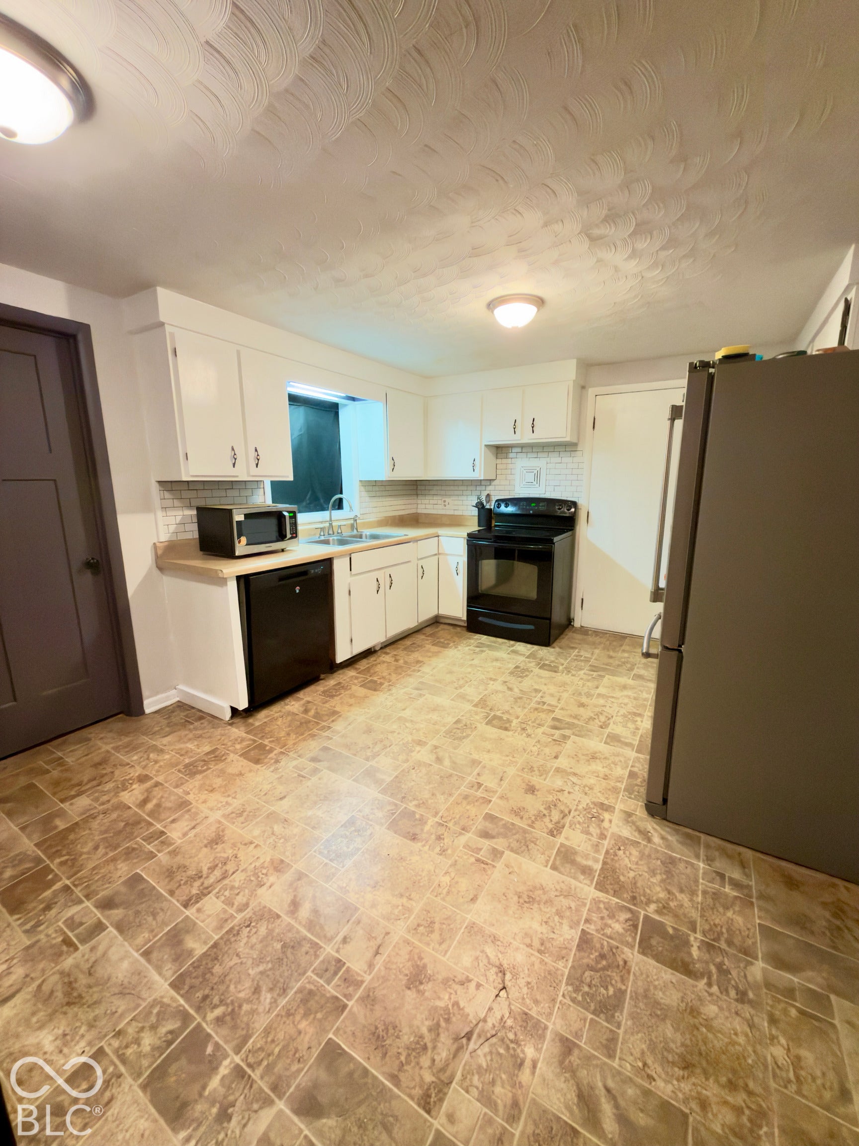 Kitchen featuring white cabinetry, solid-surface countertops, a tiled backsplash, and stone-patterned flooring