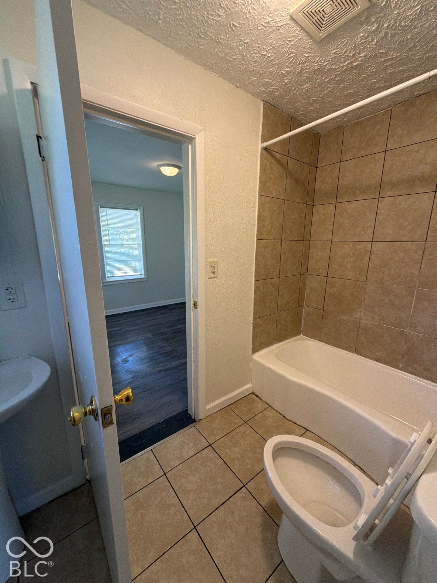 Functional bathroom featuring ceramic tile flooring, subway tile shower surround with bathtub, white porcelain fixtures, and textured ceiling detail