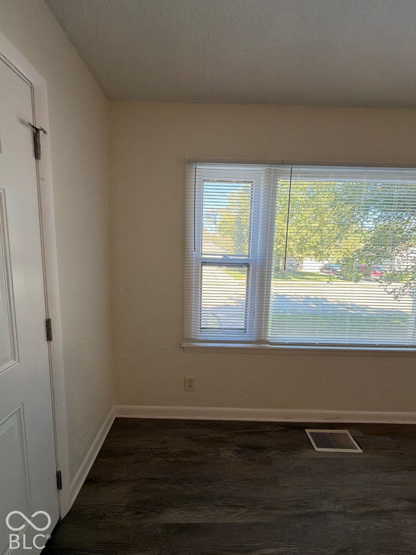 Bright corner room with expansive windows offering natural light, wood-finish flooring, and clean wall surfaces