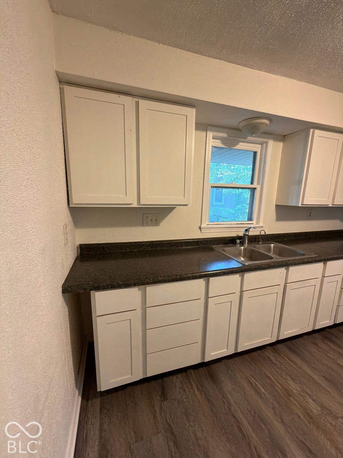 Galley kitchen featuring white shaker-style cabinetry with recessed panel doors, dark wood-finish countertops, stainless steel sink with single-handle faucet, and abundant natural light from dual windows