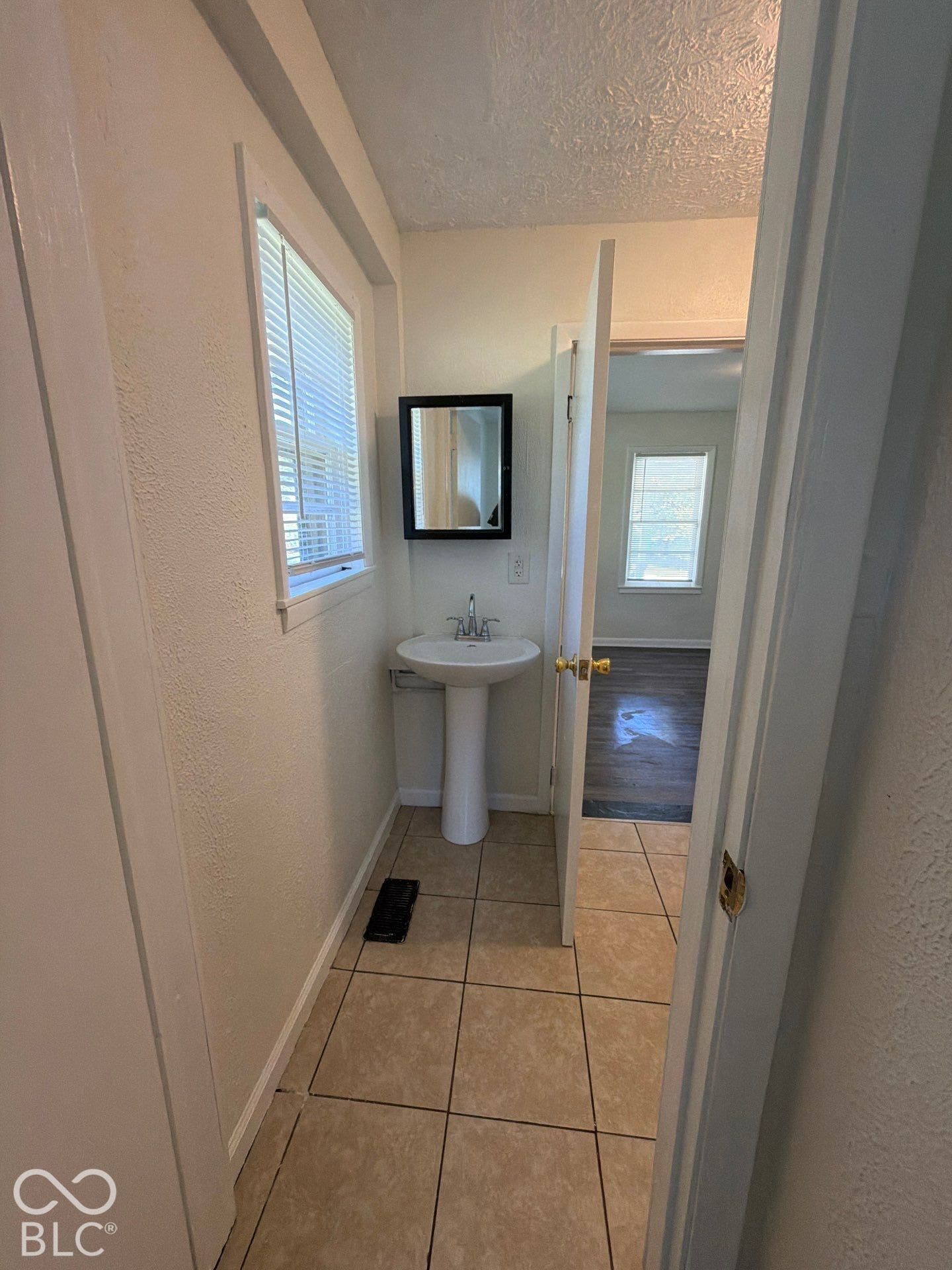 Pedestal sink with chrome faucet, framed mirror, and tiled flooring
