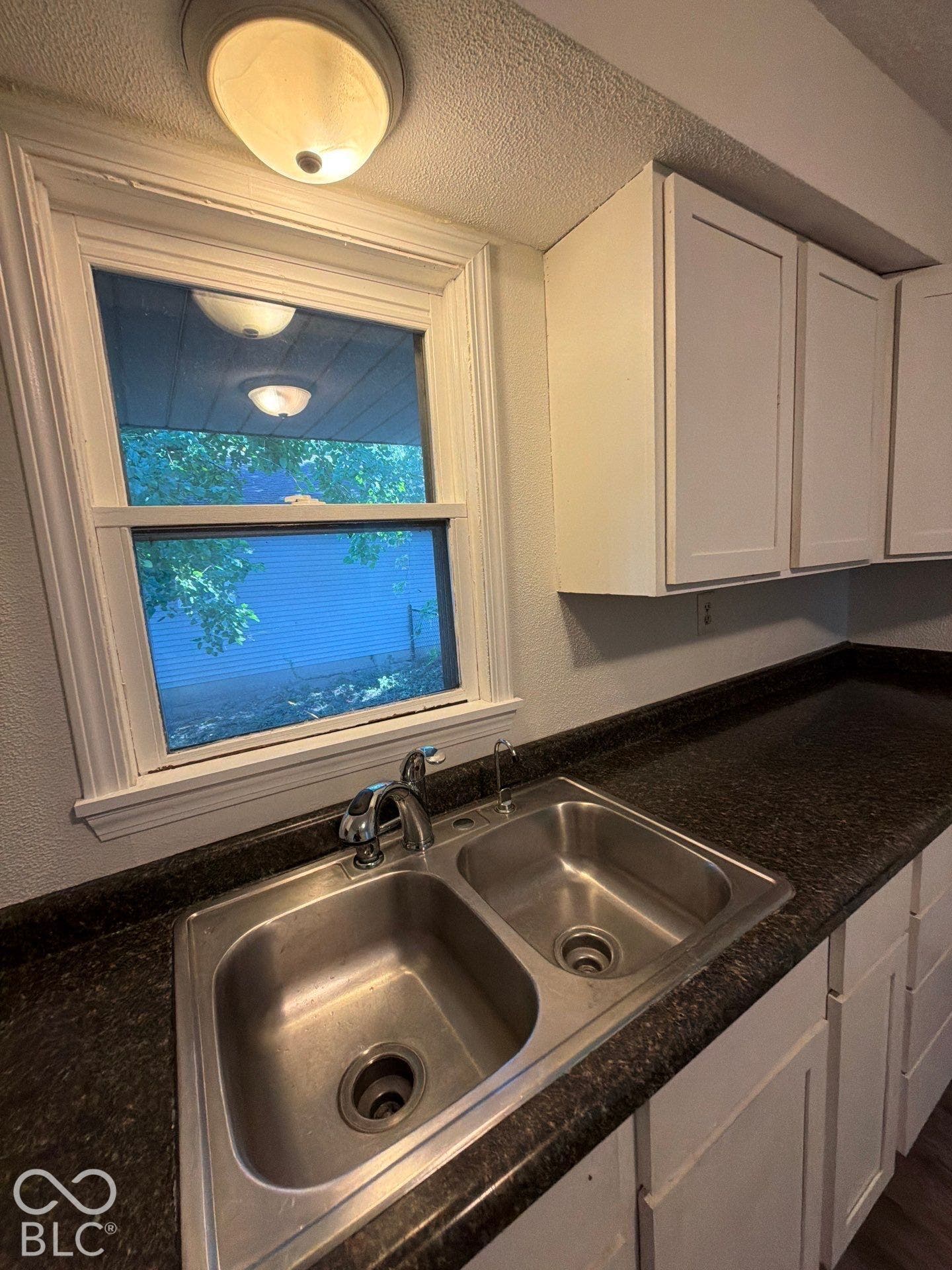 Dual basin stainless steel sink with chrome faucet, dark speckled countertop, and white cabinetry