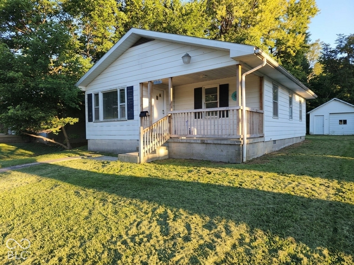 White siding exterior with a covered front porch, wood railing, and a detached garage
