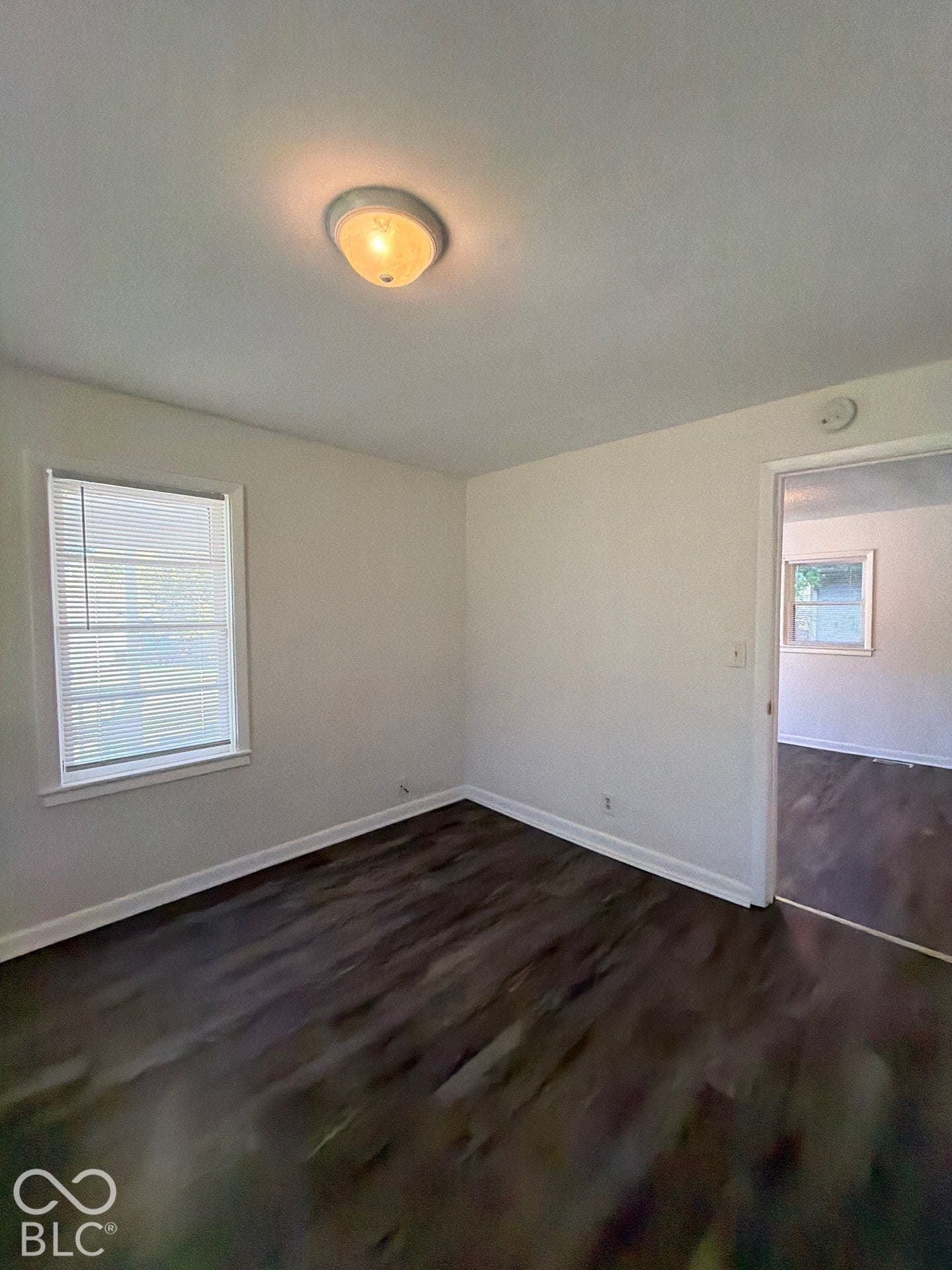 Wood-finish flooring with white baseboards, a window with blinds, and ceiling-mounted lighting