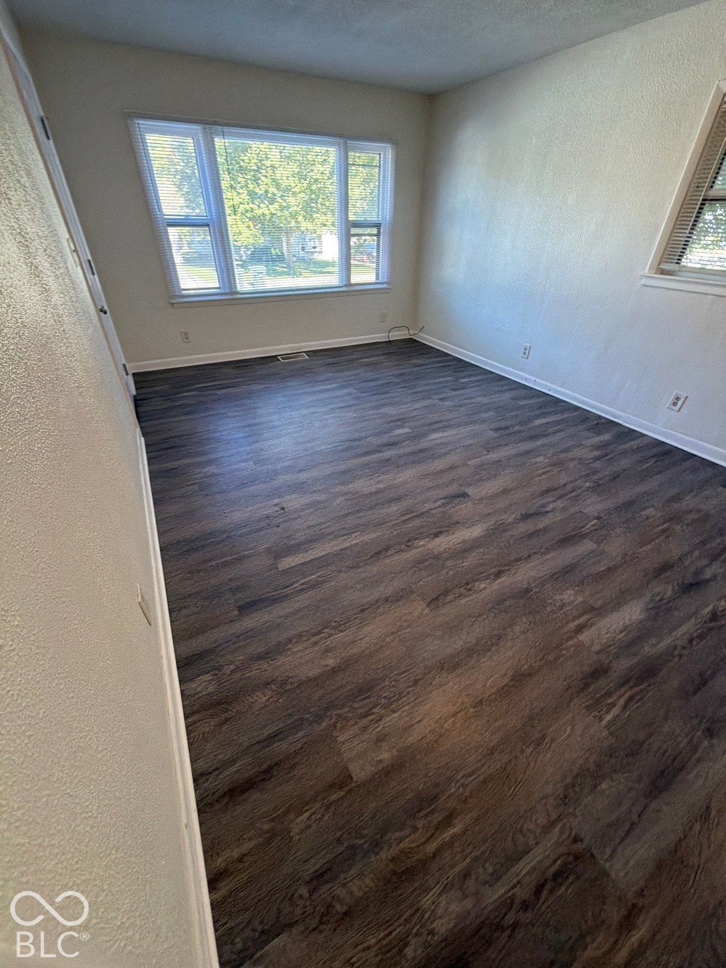 Wood-finish flooring, white painted walls, and multiple windows with blinds