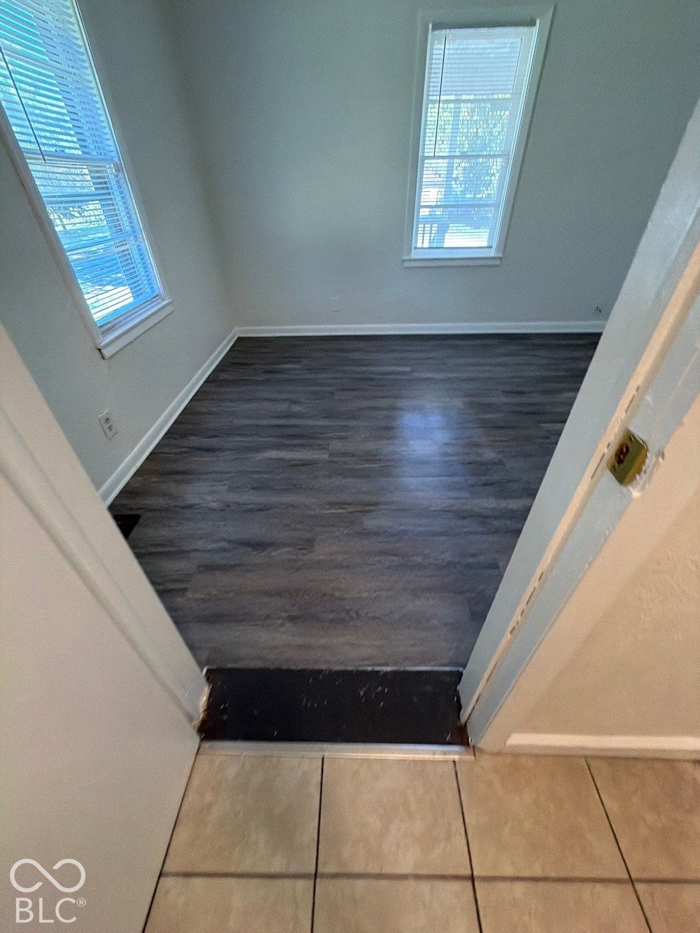 Wood-finish flooring, two windows with blinds, and white trim